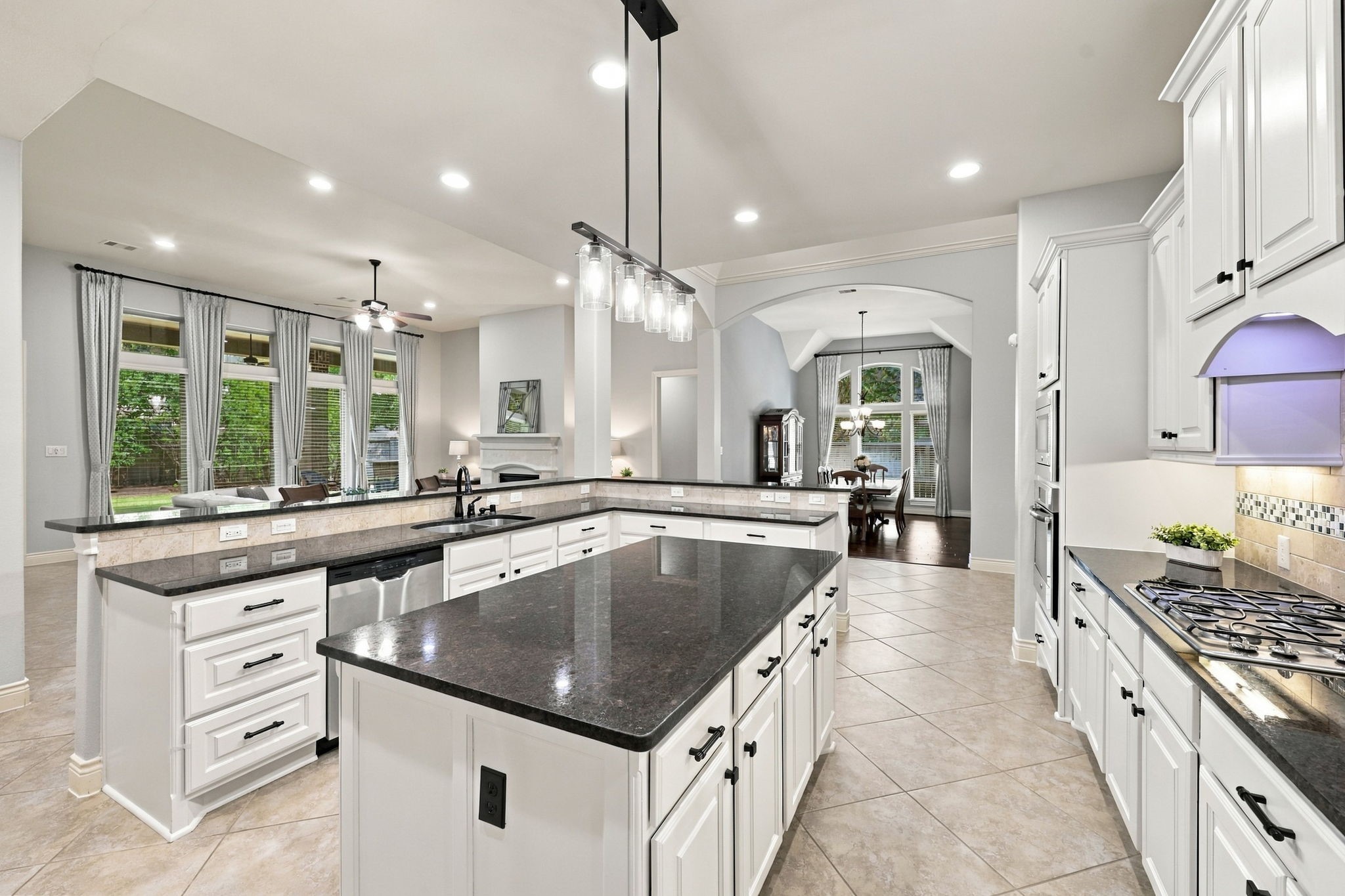 This view of the Kitchen looks back toward the Formal Dining Room and Family Room, highlighting the home's open and inviting layout. The large center island is beautifully accented by newly installed matte black pendant lights and coordinating cabinet hardware, adding a modern touch to the kitchen's timeless design.