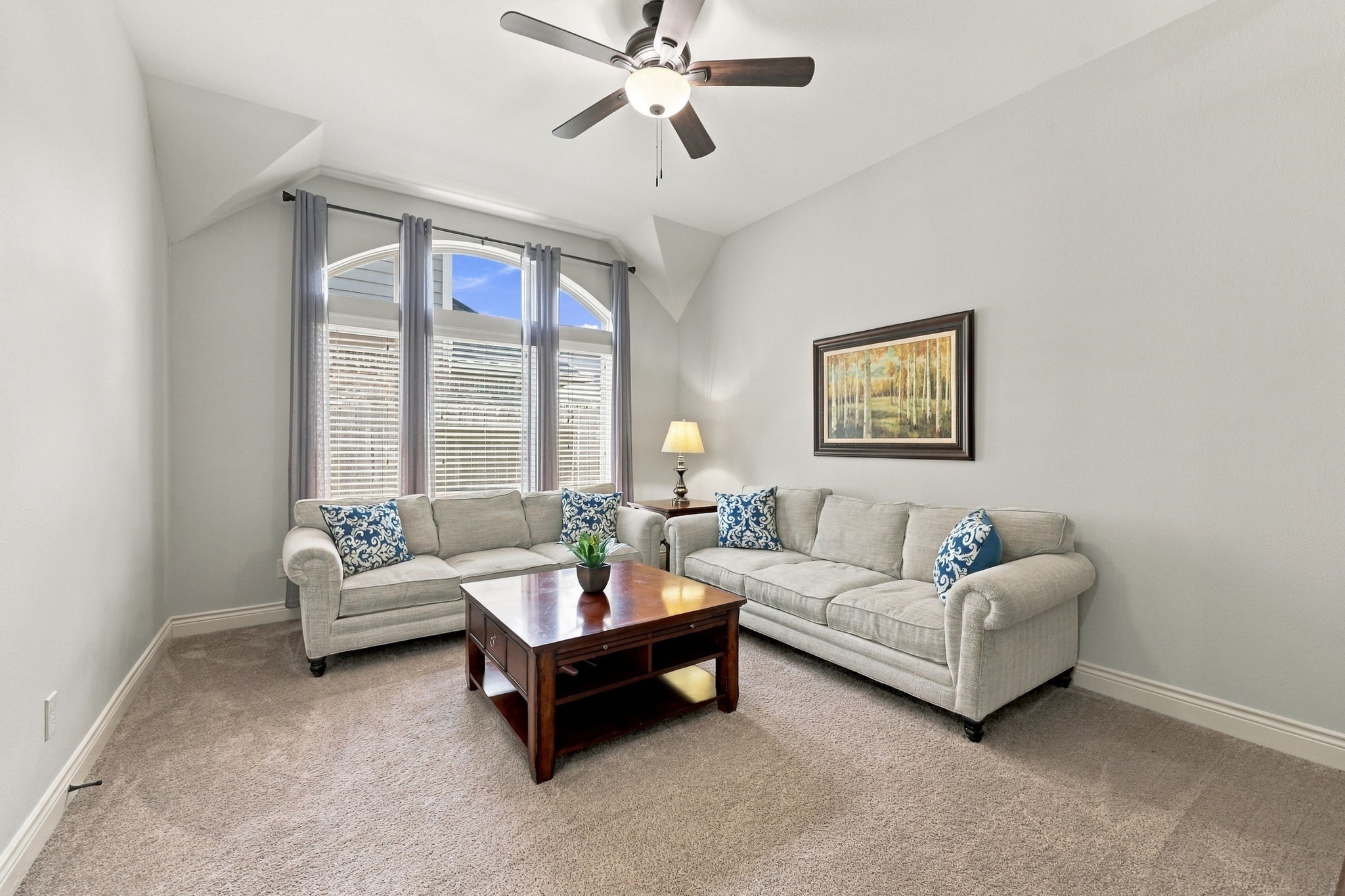 The Gameroom/Media Room features a wall of windows dressed with custom draperies, allowing natural light to fill the space. A 5-blade ceiling fan adds comfort, making this versatile room an inviting place to relax, entertain, or enjoy movie nights.