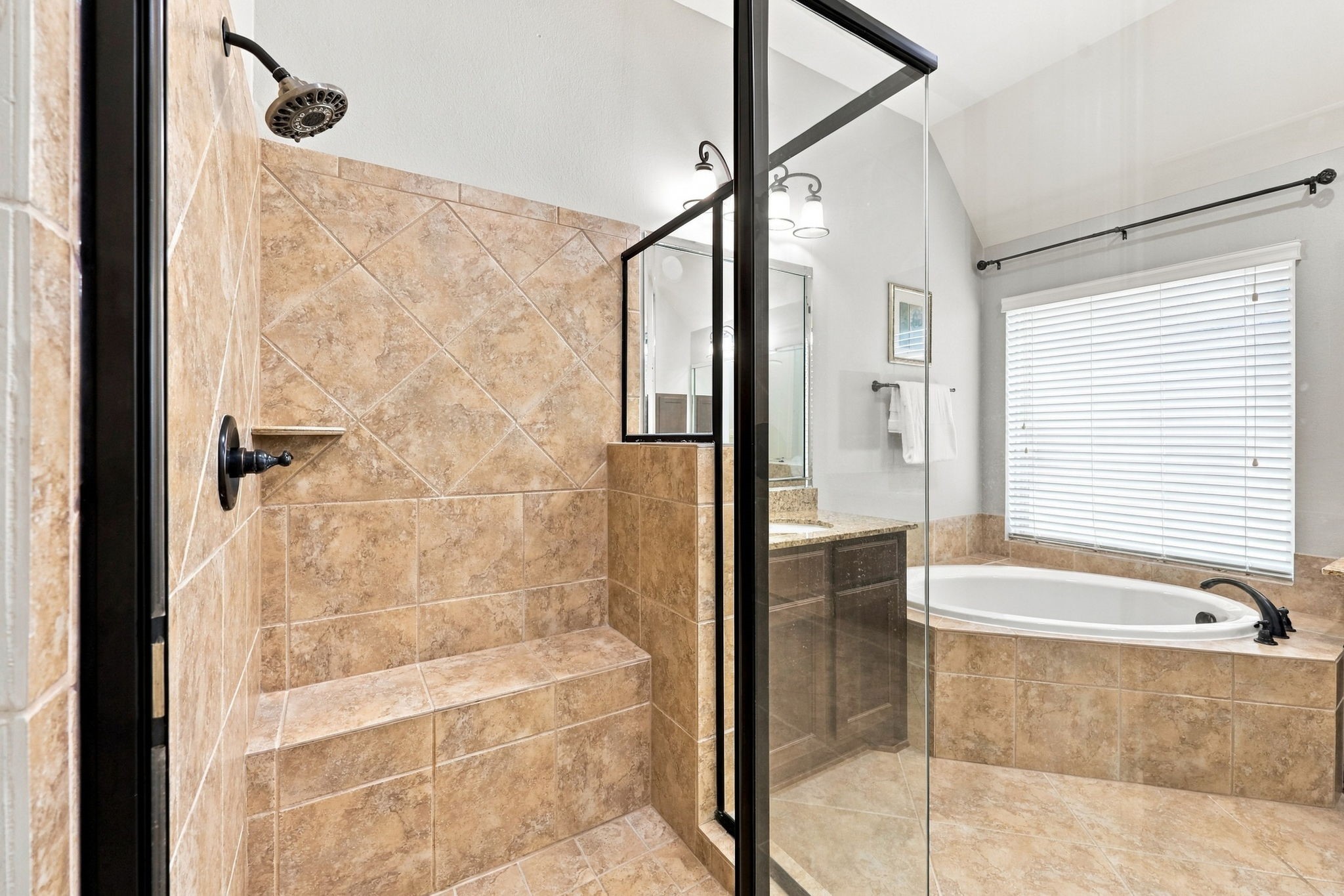 The spacious walk-in shower features a framed glass enclosure, a built-in bench, and a convenient recessed soap dish, combining comfort and functionality in the Primary Bathroom.