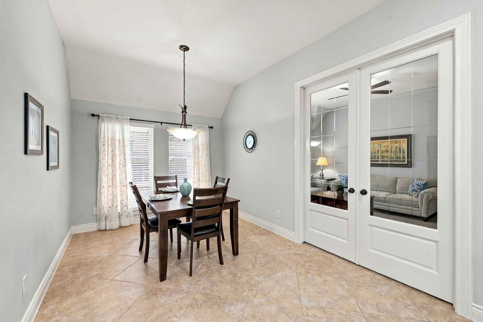 The Breakfast area features two large windows dressed with designer draperies, allowing natural light to fill the space. A beautiful wrought-iron chandelier and soothing paint colors create a warm, inviting atmosphere. Through the double glass doors, you'll catch a glimpse of the Gameroom or Media Room, adding to the home's versatile layout and entertaining options.