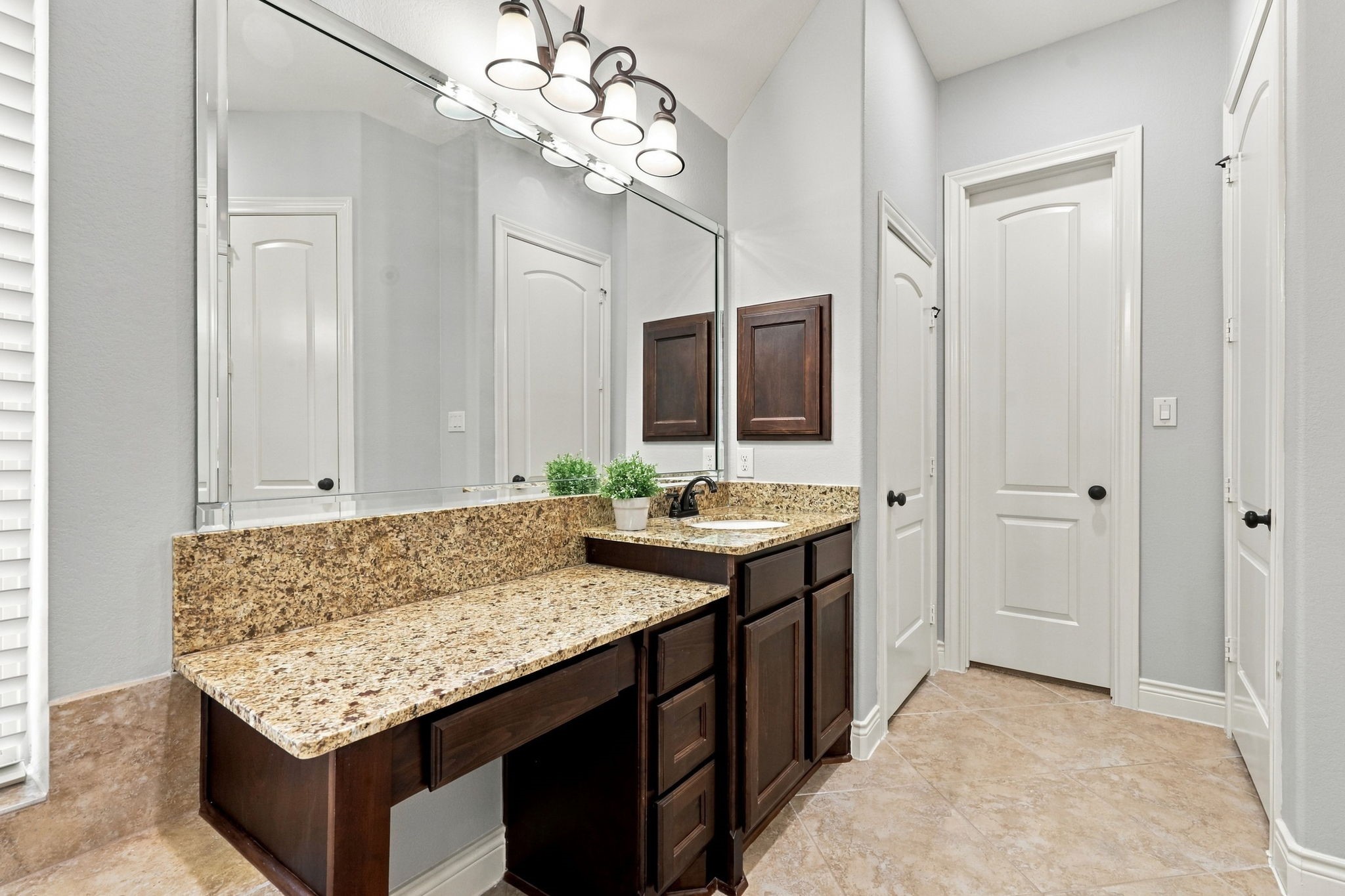 This vanity area offers additional space to sit and comfortably apply makeup, adding a touch of convenience to your daily routine. The doors in the distance lead to the second walk-in closet and a separate linen closet, providing additional storage and organization.