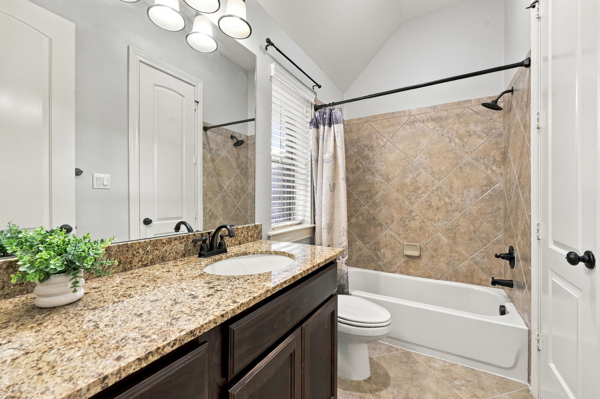 The adjoining Bathroom serves the Bedroom shown in the previous photo and features a spacious vanity with an undermount sink, rich espresso cabinetry, and coordinating oil-rubbed bronze faucets and light fixtures. A tub and shower combination offers added convenience and functionality.