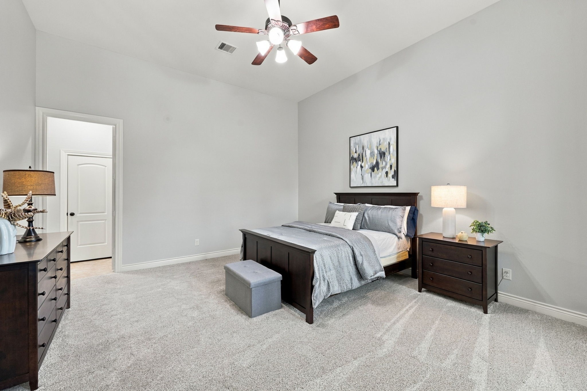 The spacious Primary Suite is privately situated at the back of the home, offering a peaceful retreat from the main living areas. Light-colored wall-to-wall carpeting and high ceilings create an open, airy feel, while the generous room size easily accommodates a king-size bed, nightstands, and multiple chests of drawers, with plenty of space to create your own relaxing sanctuary.