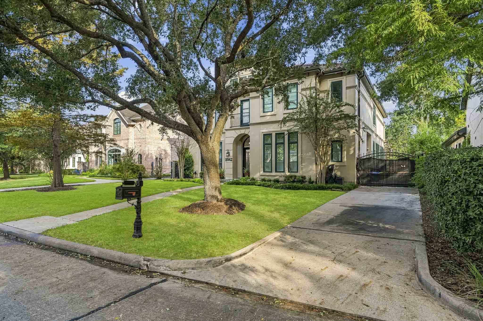 Elegant two-story home with a classic facade, framed by mature trees and lush landscaping, offering a welcoming driveway and charming curb appeal.