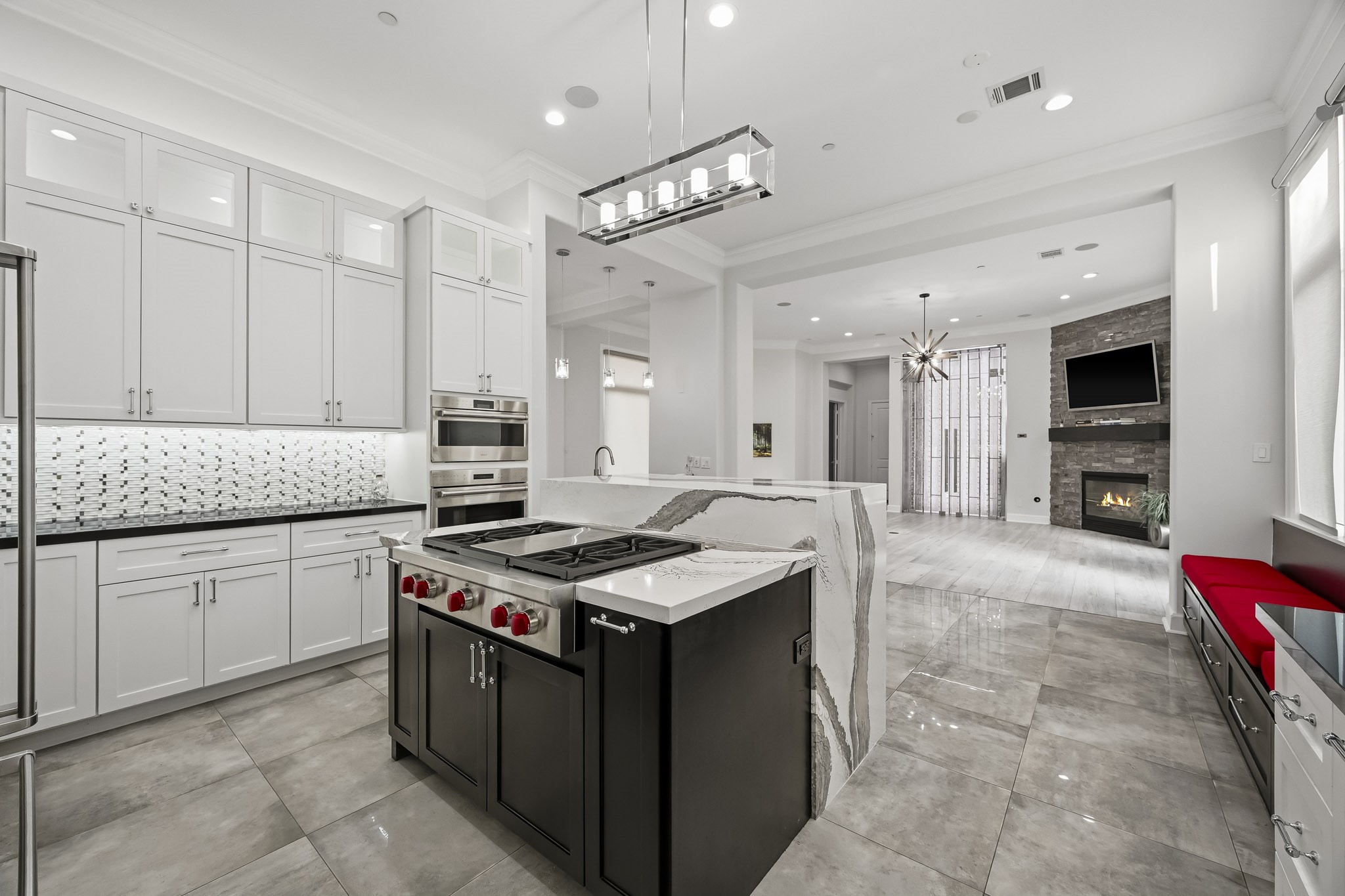 Modern kitchen featuring sleek white cabinetry, a stylish backsplash, and a spacious island with high-end appliances. The open layout flows into a cozy living area with a fireplace and ample natural light.