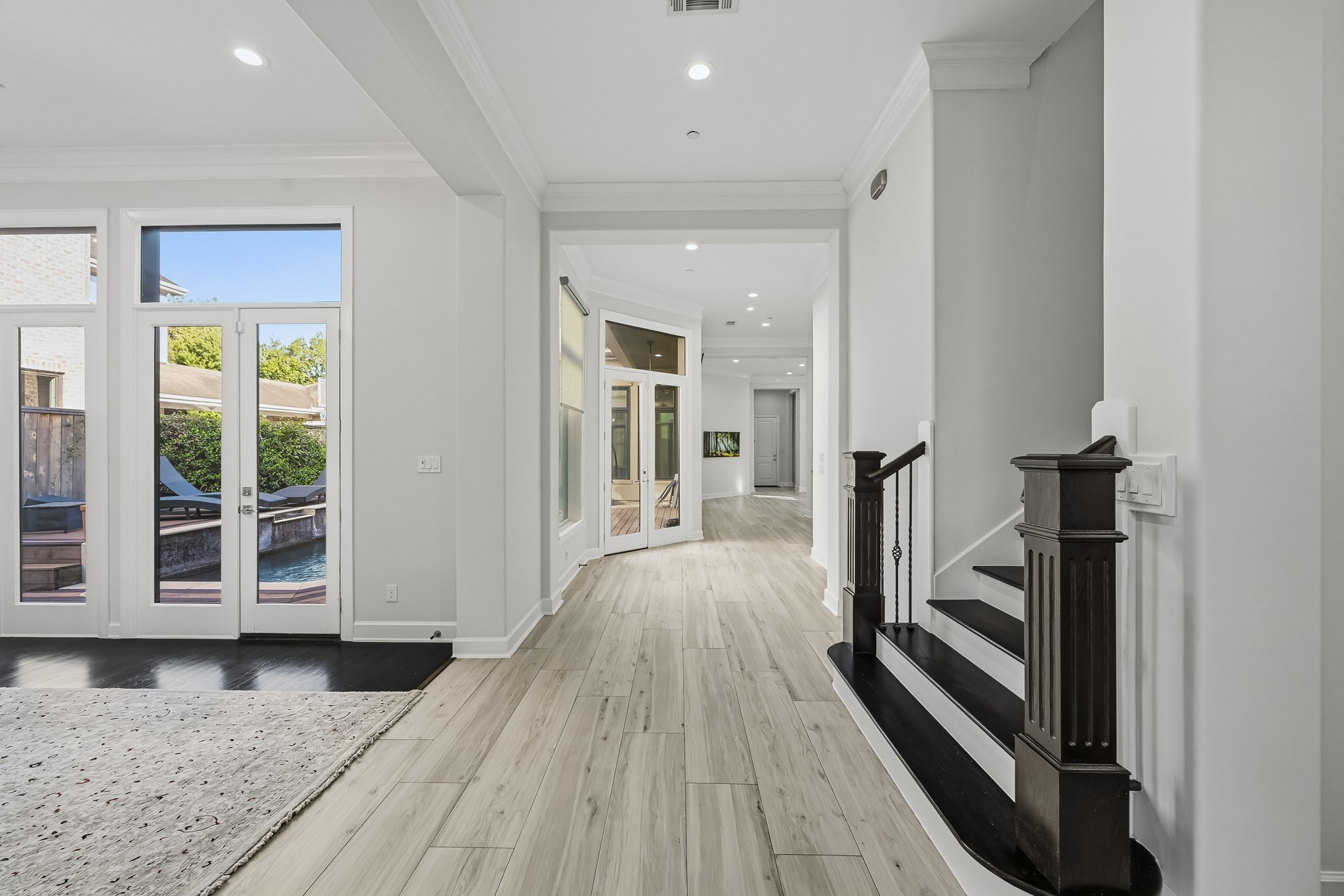 Elegant entryway with sleek floors leading to an open living space. French doors offer abundant natural light and a view of the inviting outdoor pool area.