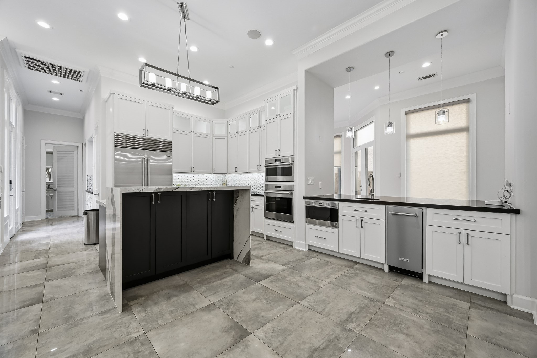 A modern kitchen featuring cabinetry, high-end stainless steel appliances, and elegant pendant lighting, complemented by a spacious island and polished tile flooring.