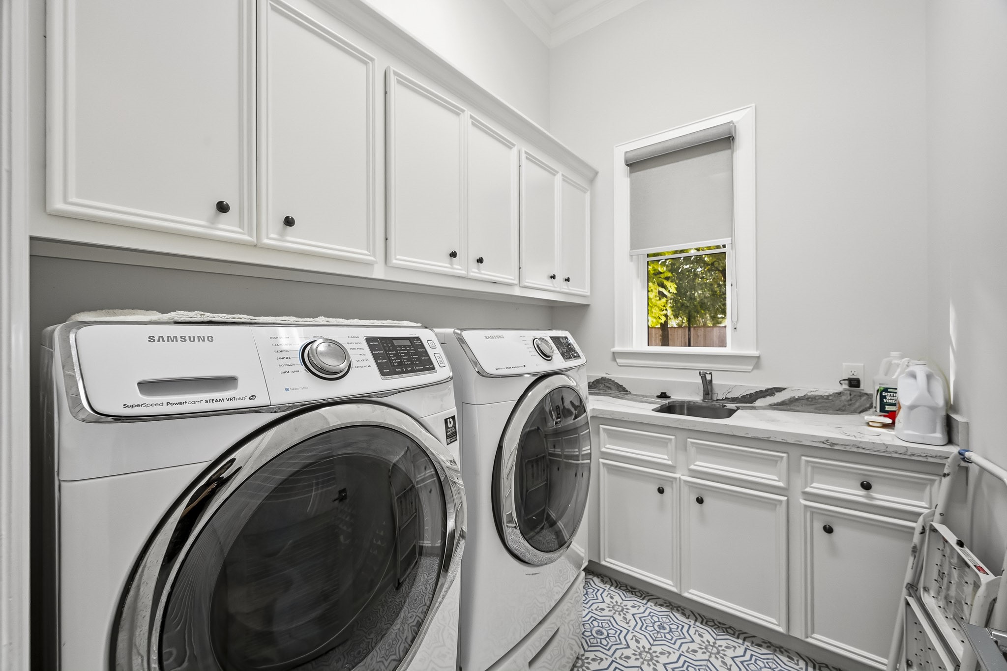 Spacious laundry room featuring modern washer and dryer, ample cabinetry, and a convenient sink area with a view.