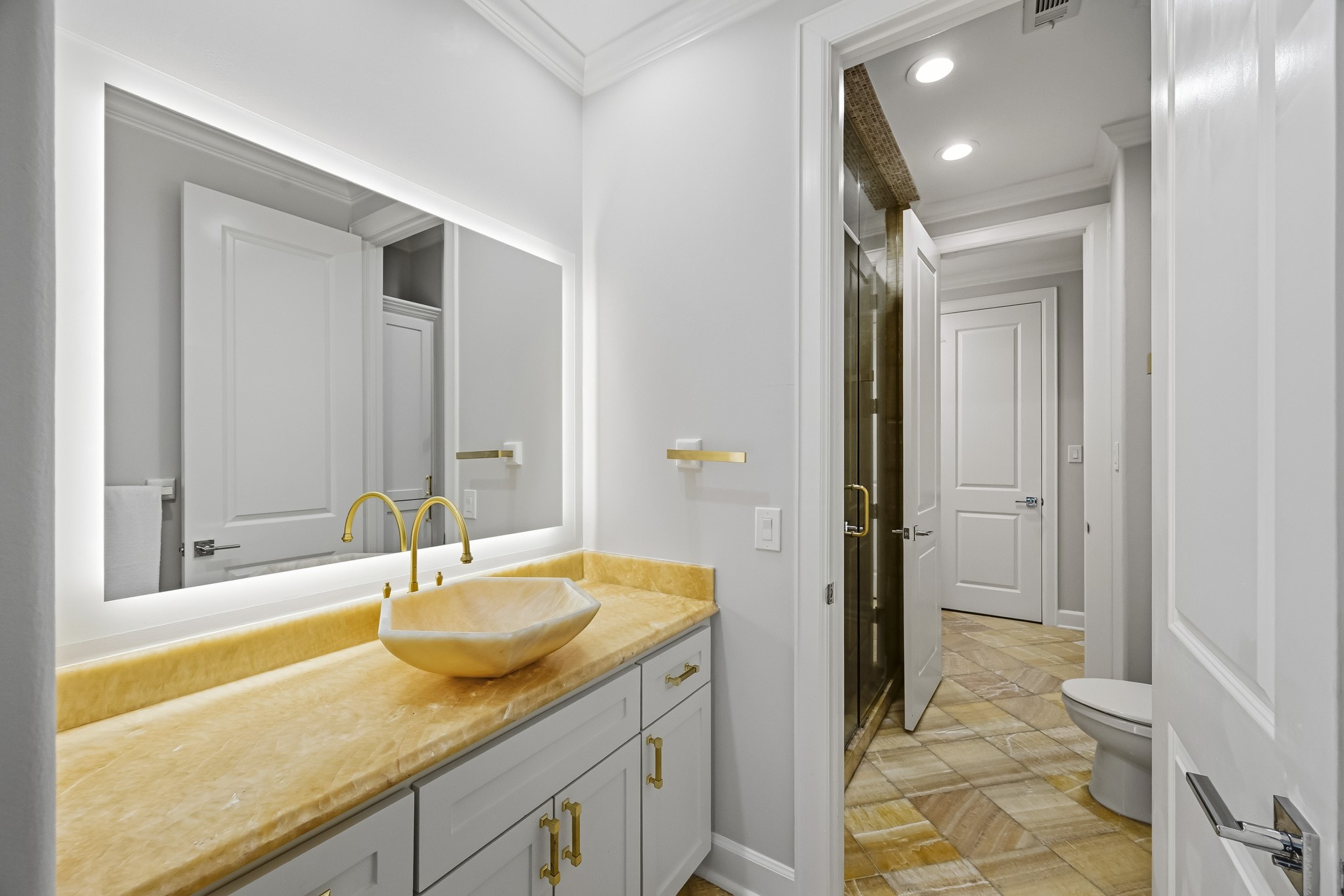 Elegant jack and jill bathroom featuring a luxurious vessel sink with a stylish gold faucet, a glowing backlit mirror, and sophisticated tile flooring.