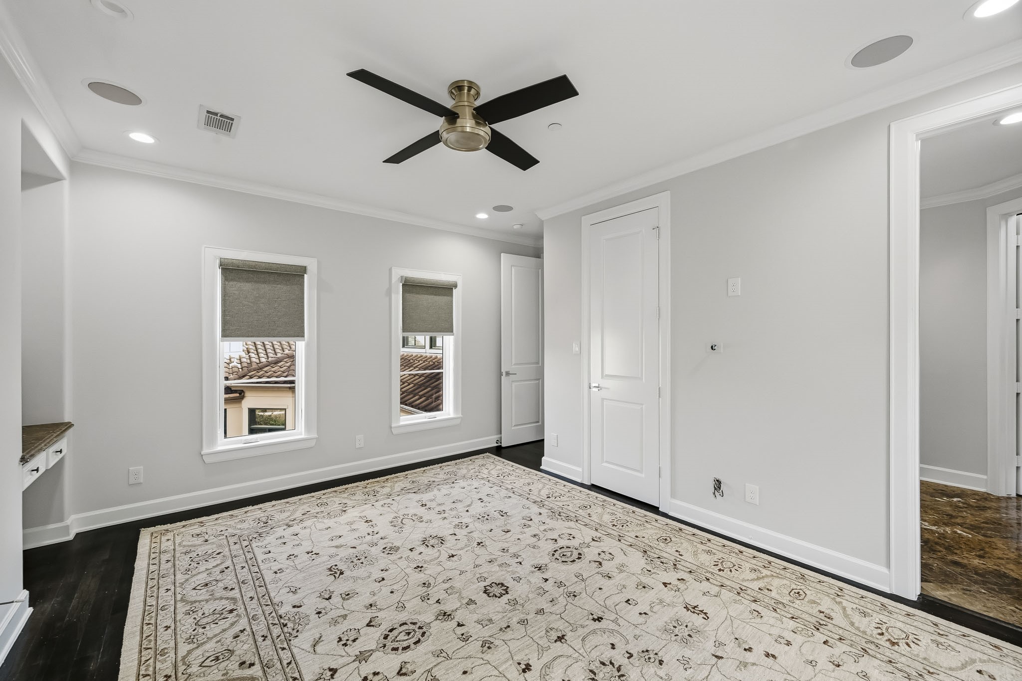 Bright and airy bedroom with elegant dark flooring, a stylish ceiling fan, and ample natural light from two windows.
