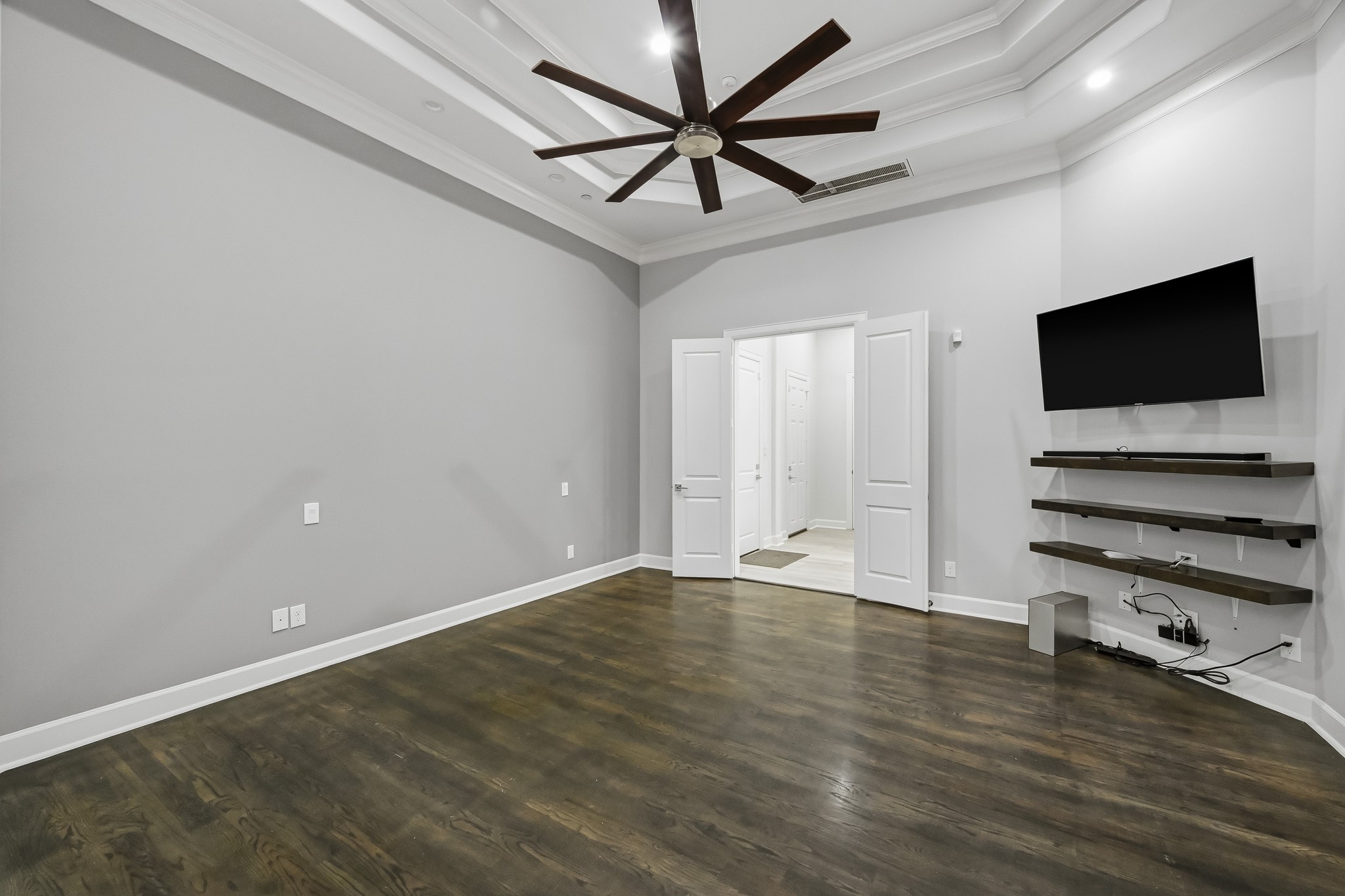 Spacious primary bedroom with an elegant tray ceiling, sleek floors, and modern built-in shelving, perfect for enjoyment.