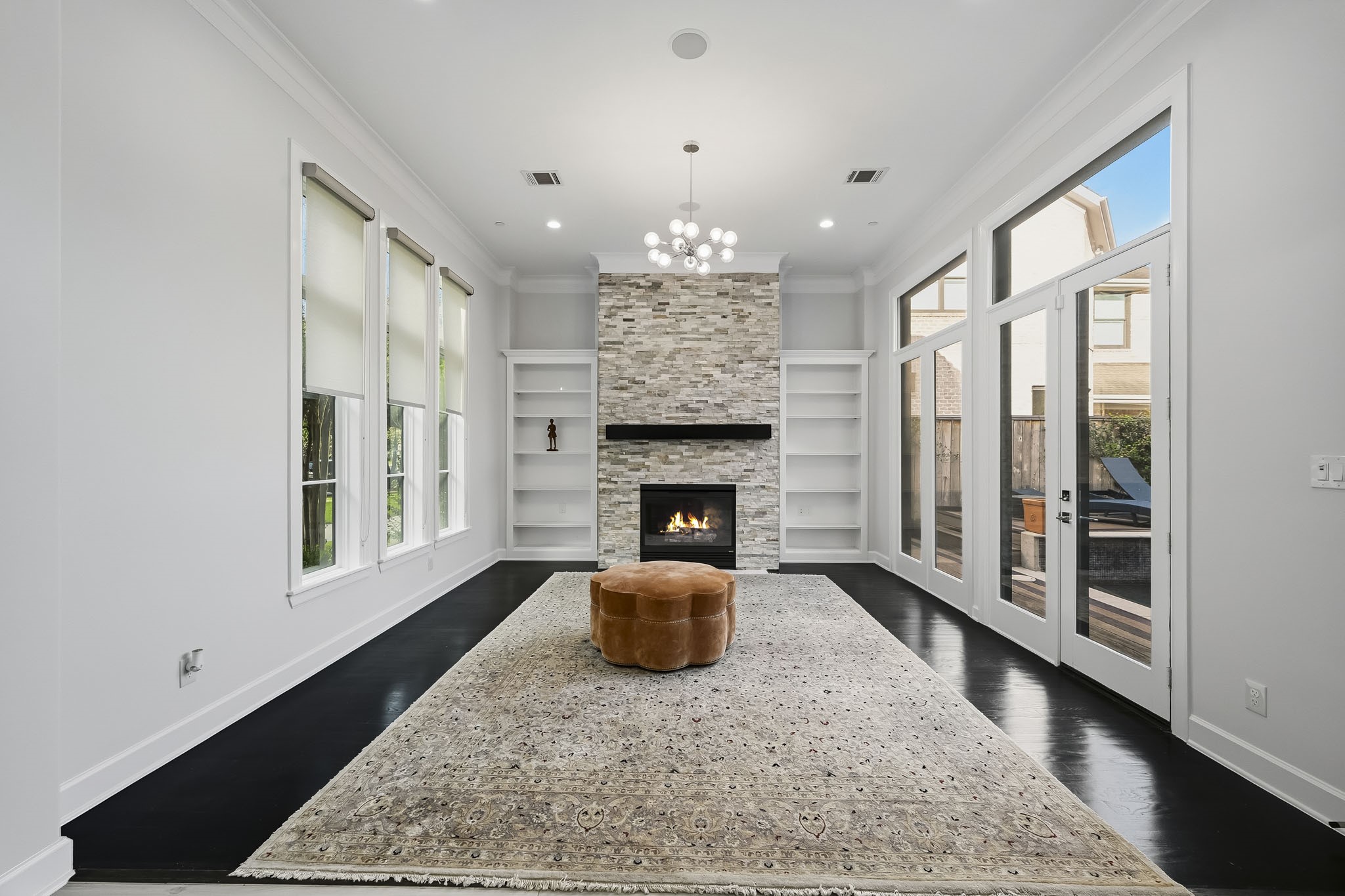 Elegant living space featuring a modern stone fireplace, expansive windows, and sleek dark flooring, creating a bright and inviting space.