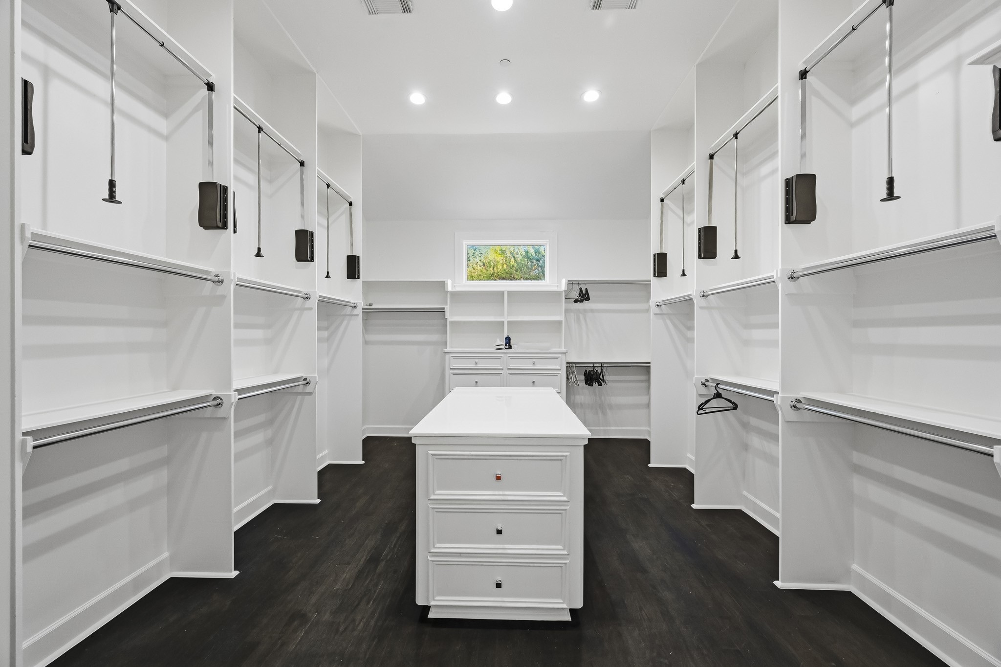 Spacious primary walk-in closet featuring sleek white cabinetry, ample hanging space, and a central island for added convenience and organization.