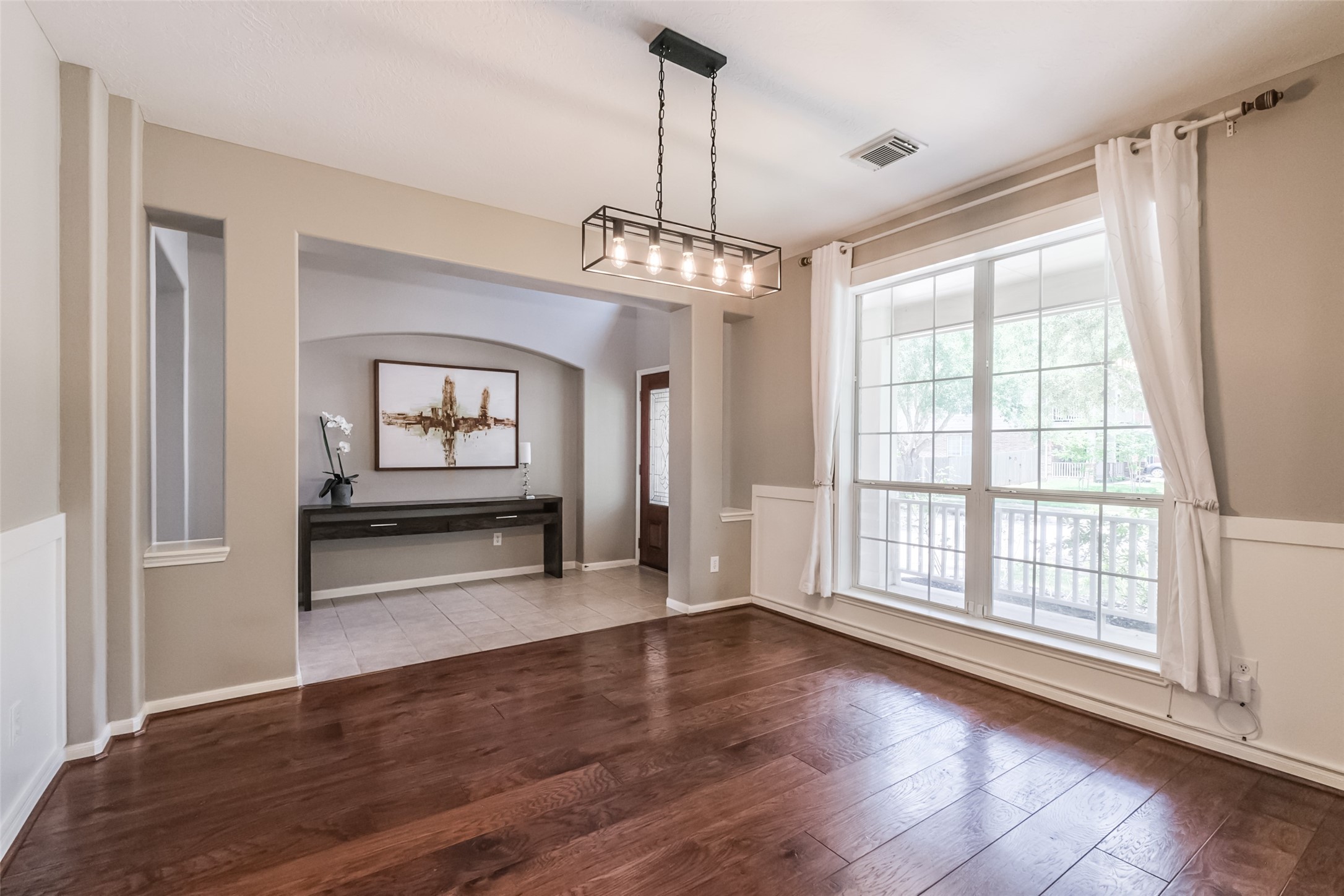 Bright dining area with hardwood floors, large window, stylish light fixture.