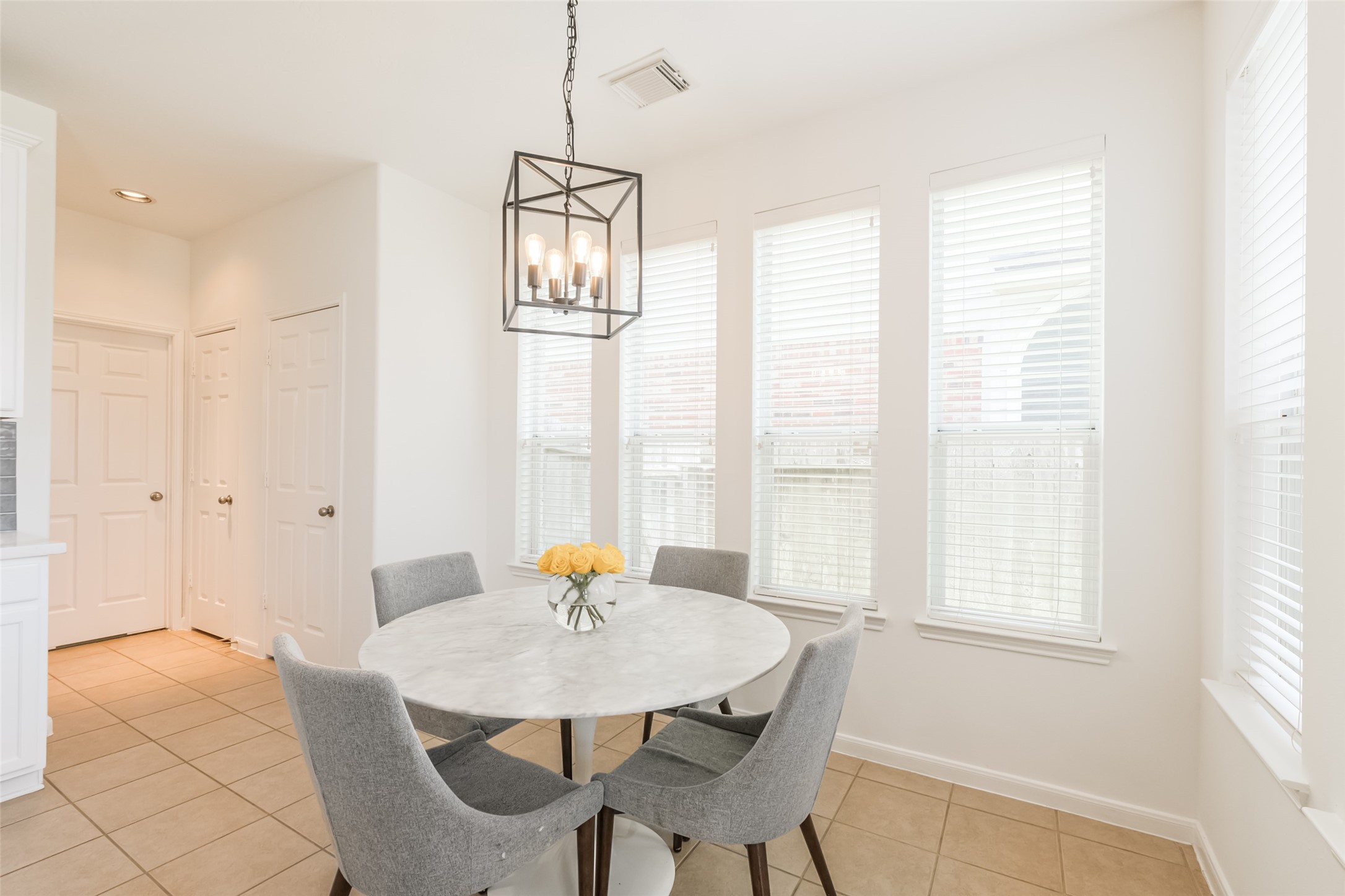 Bright dining area with large windows, neutral tile flooring, and a modern chandelier.