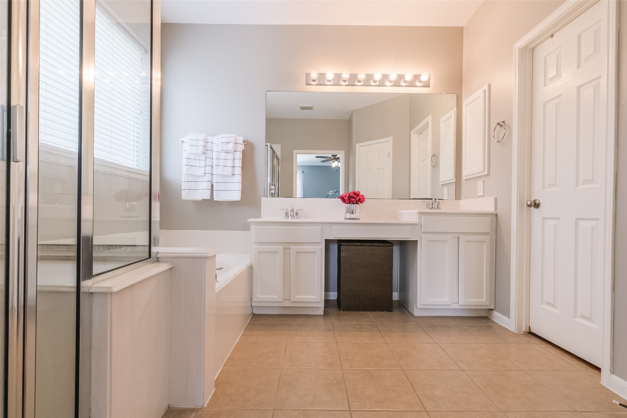 This bathroom features a spacious layout with a large mirror and dual sinks on a white vanity. It includes a separate shower, a soaking tub, and ample lighting, creating a bright and inviting space.