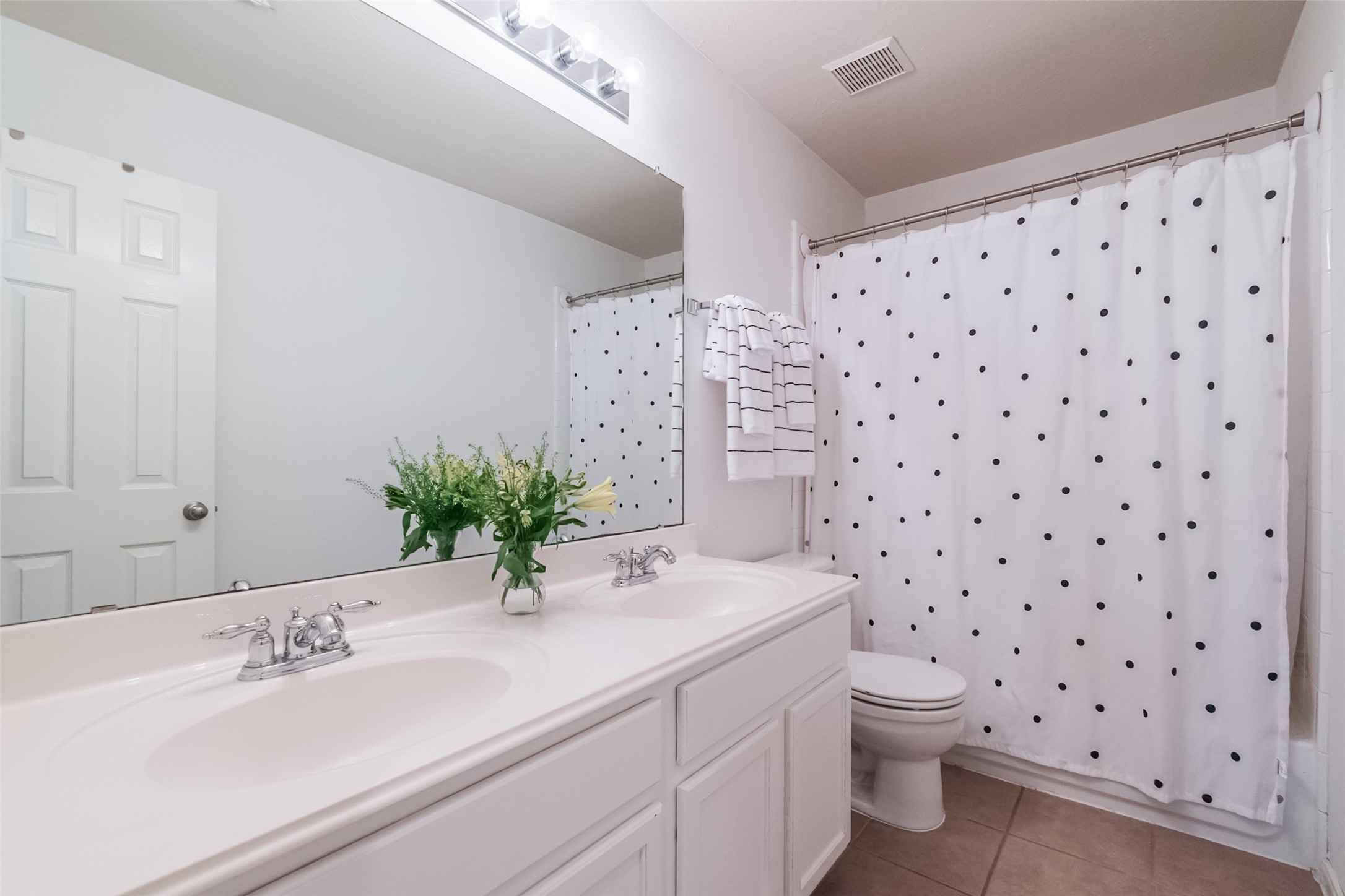 Bright and clean bathroom featuring a double sink vanity, white cabinetry, tub/shower combination.