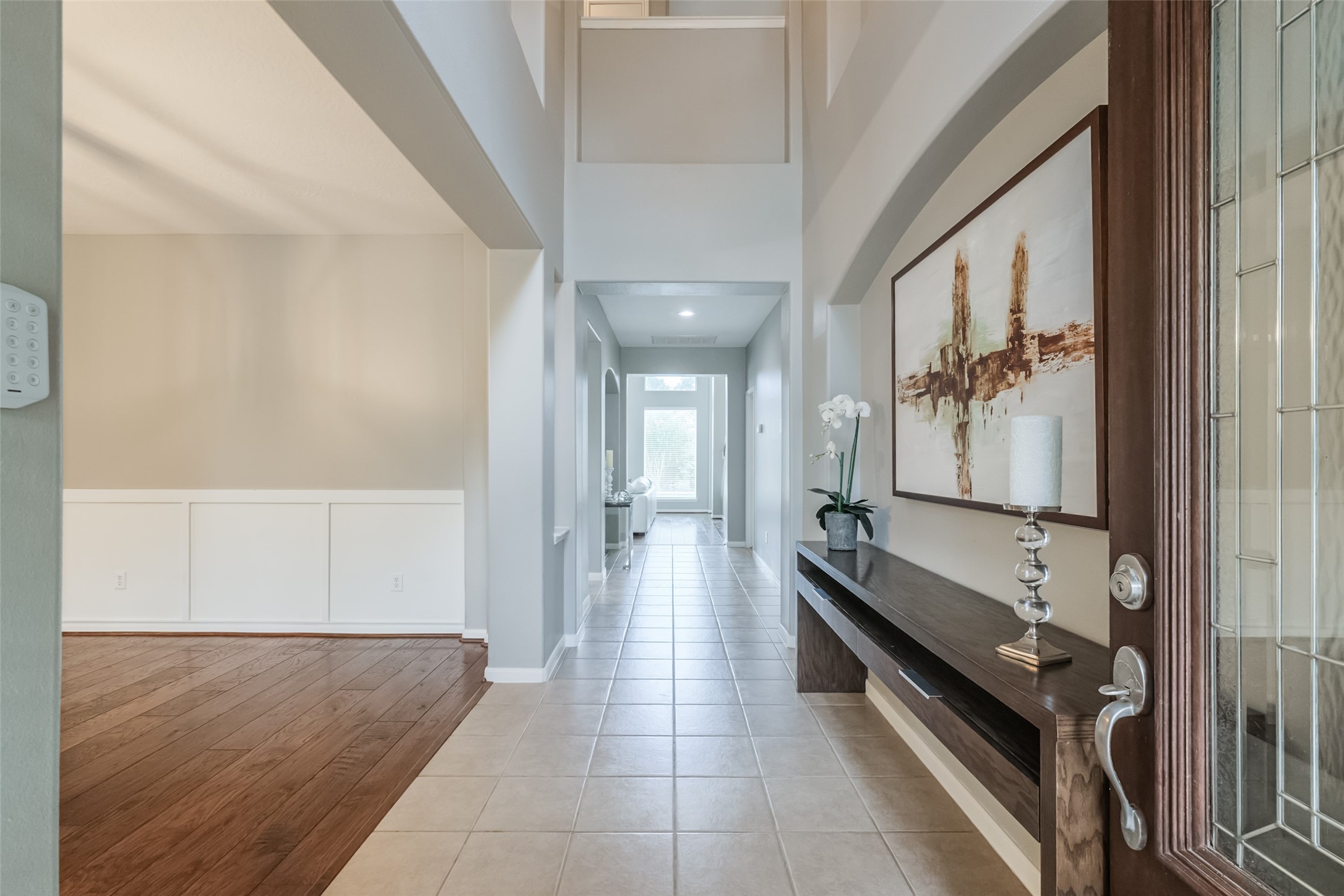 This inviting entryway features high ceilings, a mix of tile and wood flooring, and a long hallway leading to a bright, open space.