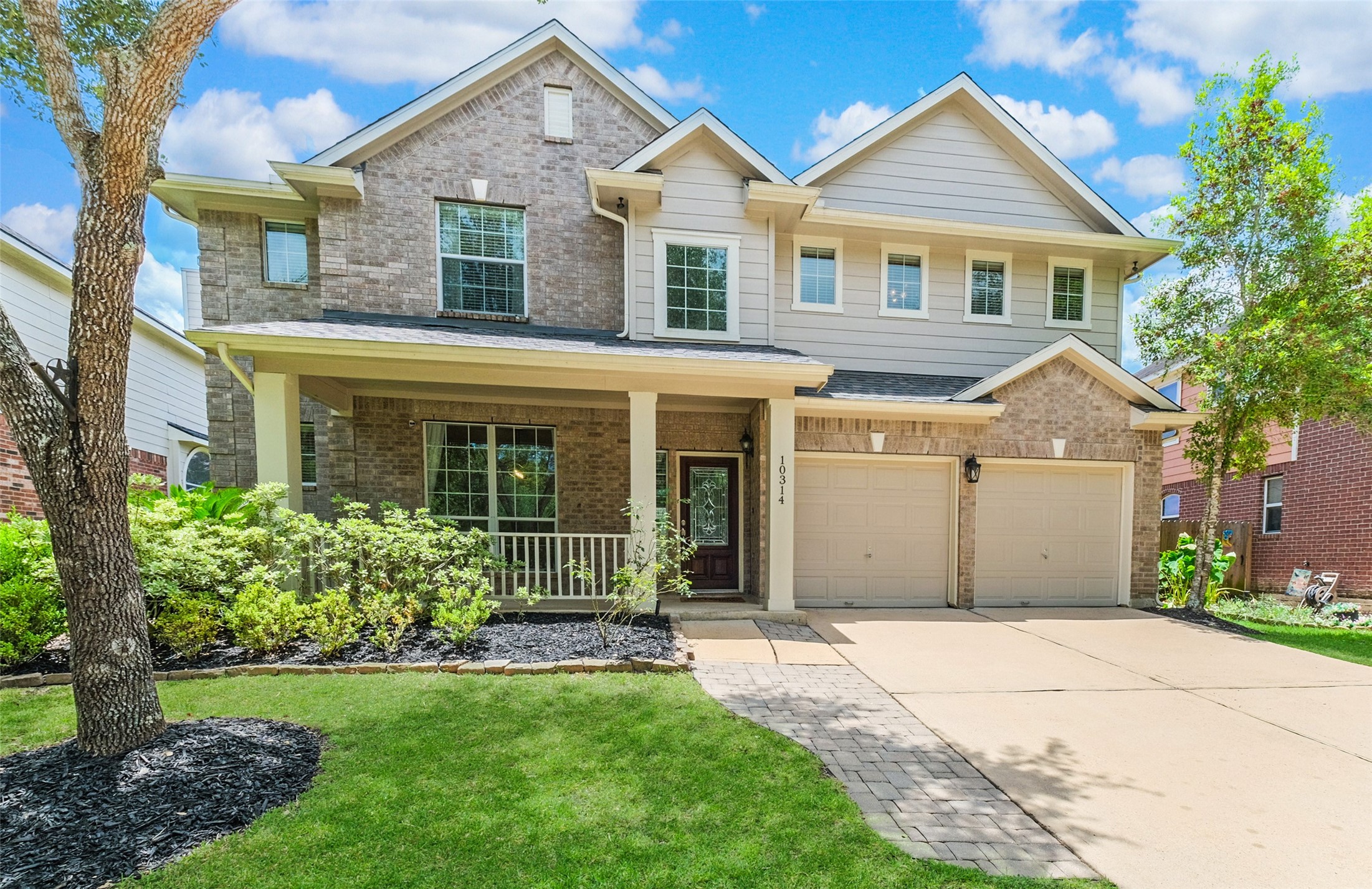 This two-story home features a charming brick facade with a welcoming front porch. It has a well-maintained lawn, a double garage, and large windows that provide ample natural light. Perfect for families seeking a spacious and inviting property.