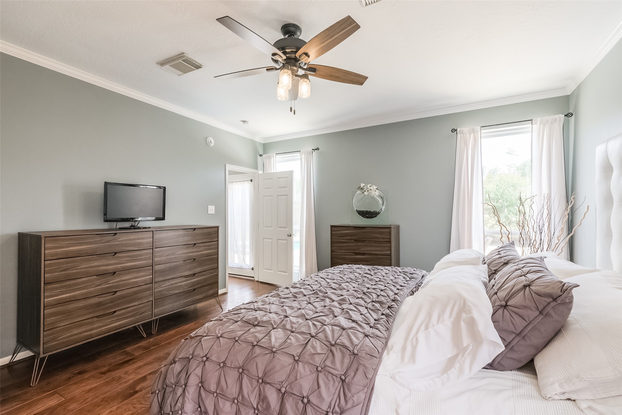 This primary bedroom features hardwood floors, a ceiling fan, and soft gray walls.