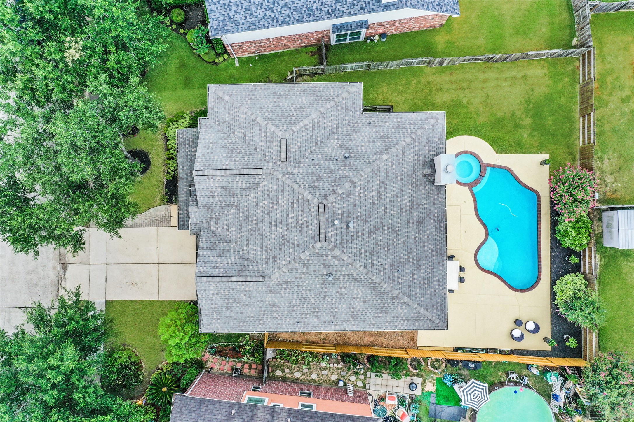 This aerial view showcases a well-maintained home with a spacious backyard, featuring a uniquely shaped pool and spa. The property is bordered by a lush green lawn and mature trees, providing privacy and a serene outdoor space.