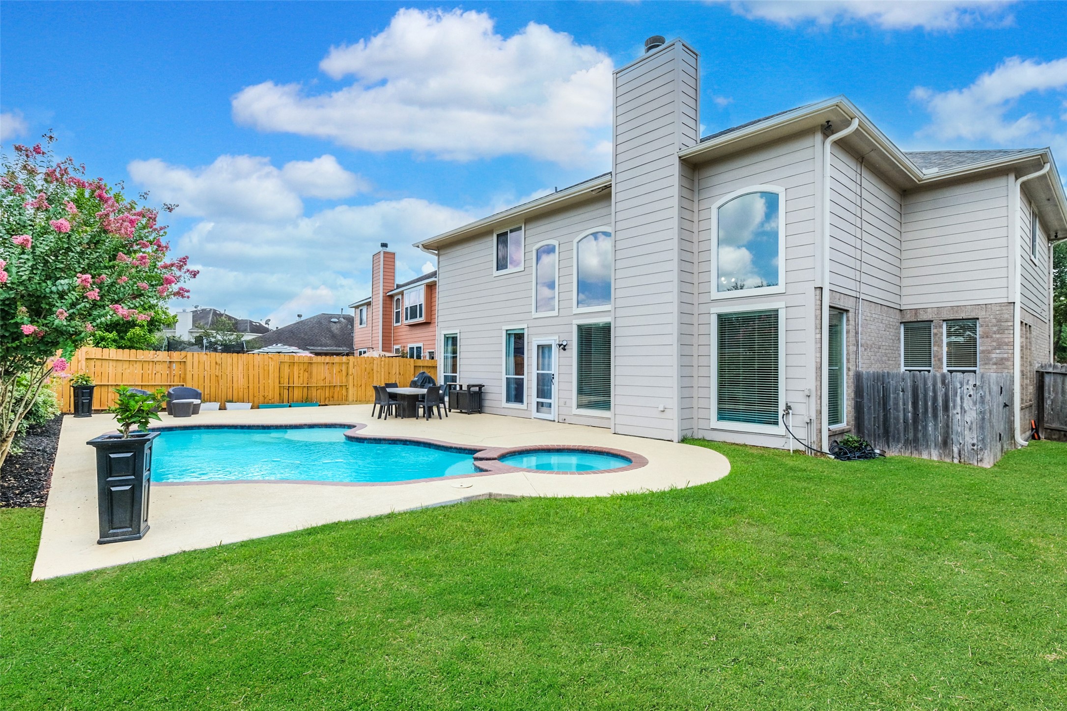 This spacious backyard features a pristine pool and hot tub, surrounded by a well-maintained lawn and privacy fence. The modern two-story home has large windows, offering plenty of natural light. Perfect for outdoor entertaining and relaxation.
