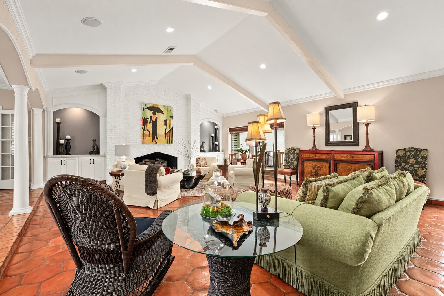 Beautiful architectural details take center stage with a striking brick fireplace, custom built-in cabinetry, graceful arched niches, and elegant columns. The vaulted beamed ceiling and thoughtfully designed seating areas add warmth and character to this exceptional living space.