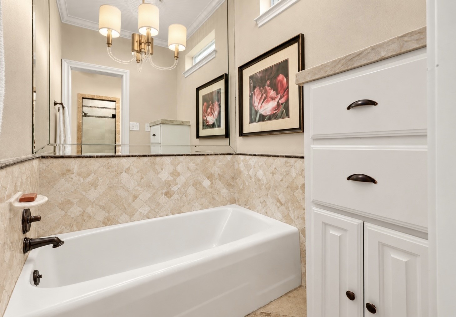 Private soaking tub area features beautiful travertine tile with elegant marble trim and a large, beveled mirror. Custom cabinetry includes a convenient pull-out dry-cleaning hamper.