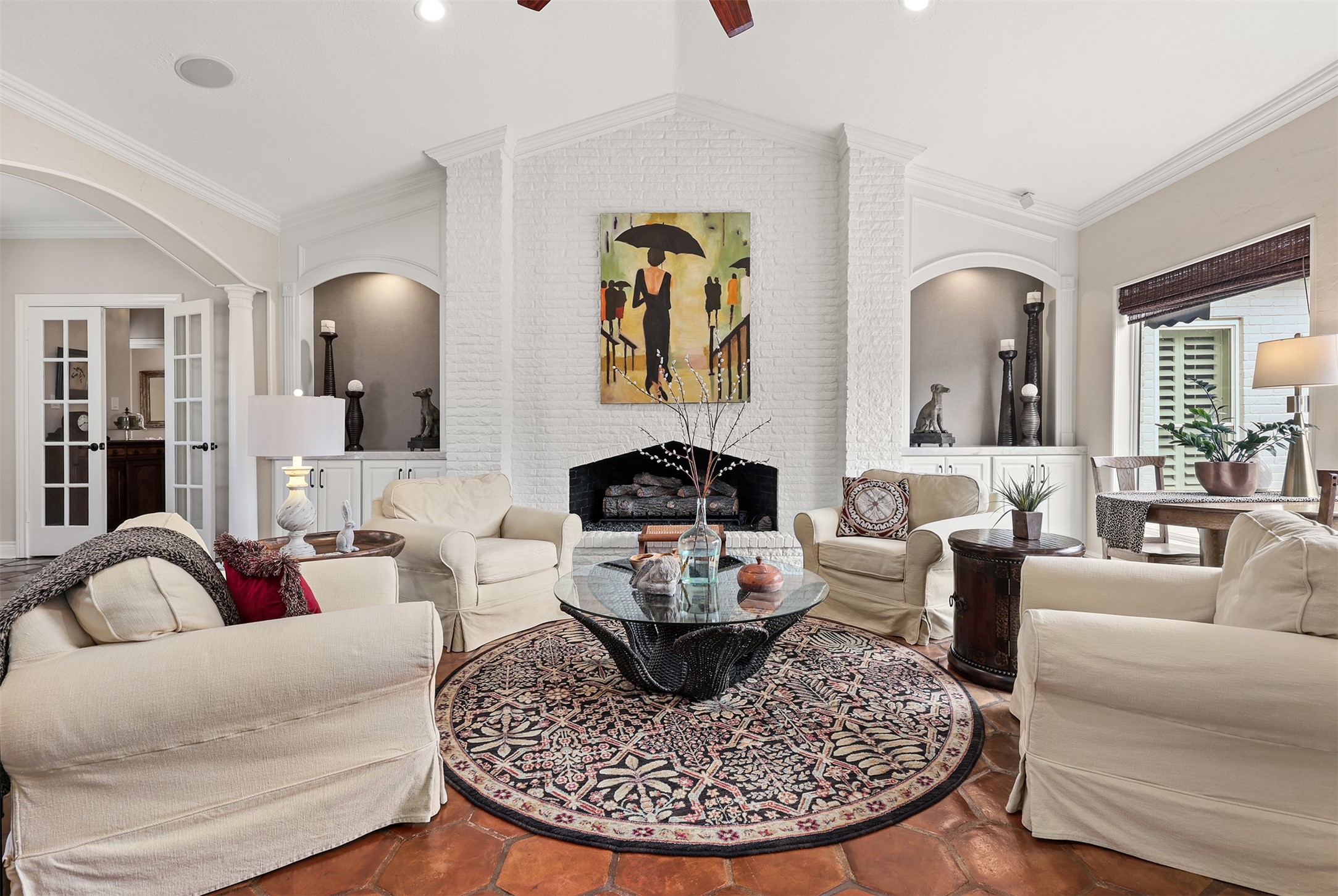A stunning floor-to-ceiling painted brick fireplace serves as the focal point of this beautiful living space, featuring an impressive four-foot custom size gas log set. Flanked by graceful arched niches and custom cabinetry, this striking fireplace adds timeless character and warmth to the heart of the home.