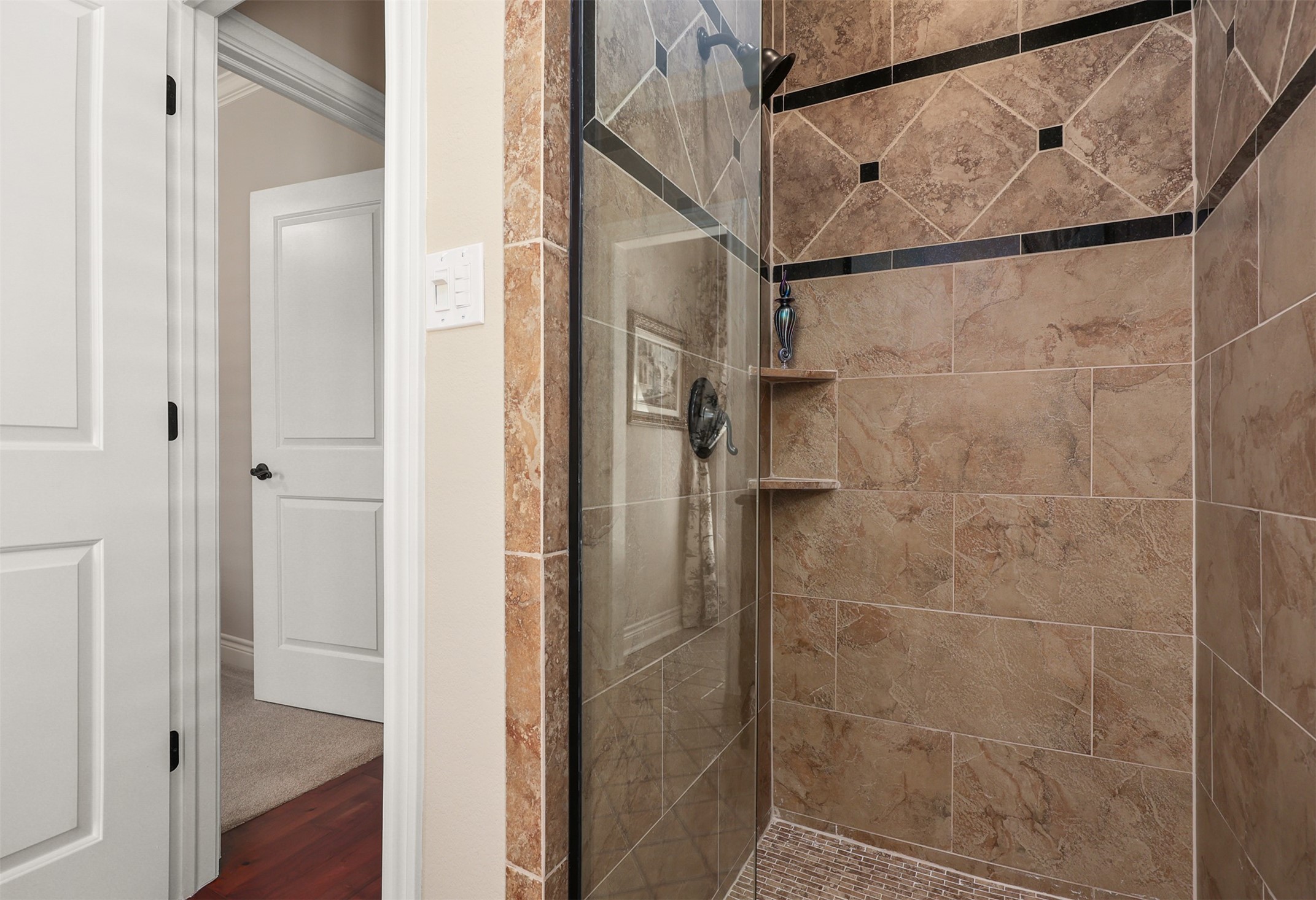 The adjoining bath to bedroom #1 features a spacious walk-in shower with beautiful custom tilework and a sleek, frameless glass shower door.