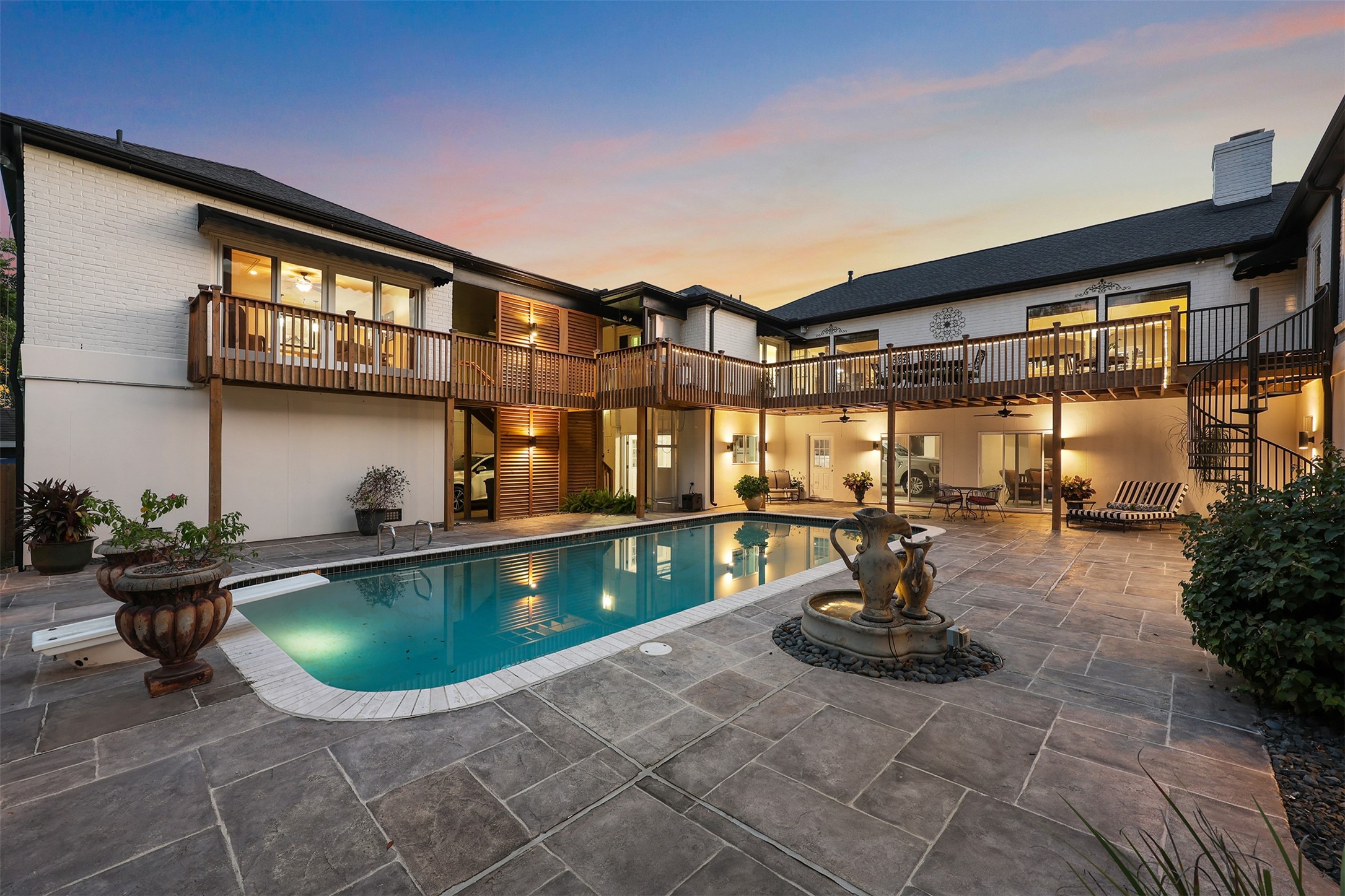 A stunning evening view captures the beauty of this exceptional outdoor retreat! Warm architectural lighting highlights the stained wood louvers, while four expansive picture windows overlook the sparkling pool from the home's main living area. The charming spiral staircase, elevated decks, and inviting pool house create a spectacular setting for entertaining or relaxing uncer the stars.