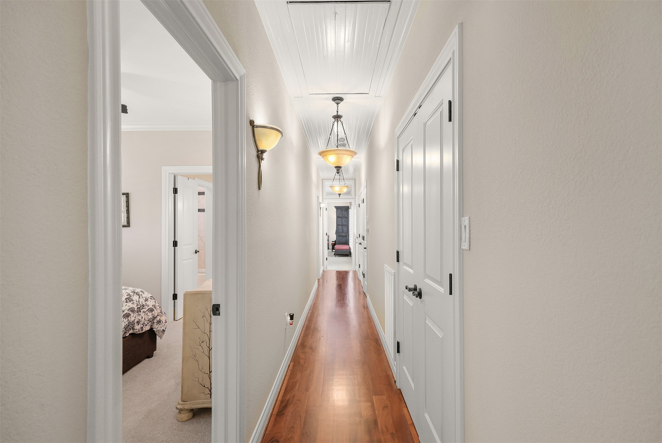 This beautiful hallway features solid mesquite wood flooring, decorative beadboard ceiling detailing, elegant lighting, and abundant storage, including a walk-in cedar closet. Bedroom #2, located to the left, has access to a full bath that can also serve the adjoining room, currently used as an office. Another example of the thoughtful custom details found throughout this home.