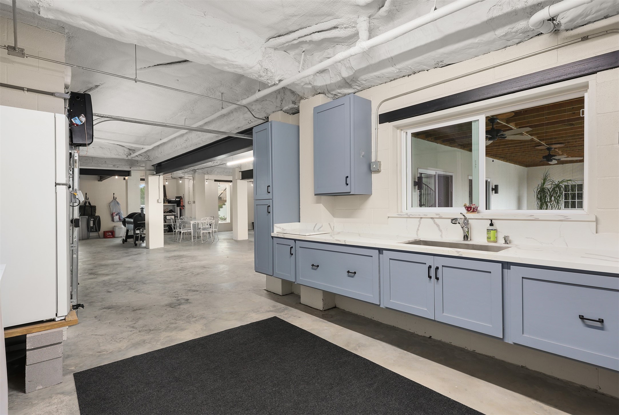 This spacious ground-level area features charming blue cabinetry, quartz countertop, and a large stainless-steel sink. the entire area beneath the home has been painted to complement the exterior, creating a bright, airy atmosphere. Update PVC plumbing beneath the home adds to the many thoughtful improvements.