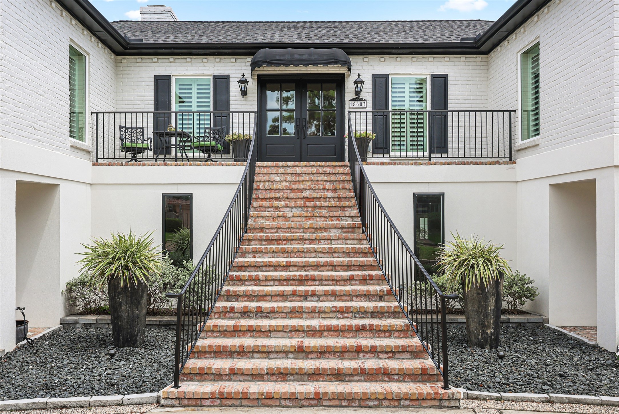 A grand brick staircase with classic wrought-iron railings welcomes you to this beautifully designed home. Elegant black double entry doors, charming lantern lighting, plantation shutters, and an inviting front porch create a timeless entrance filled with character and Southern charm.