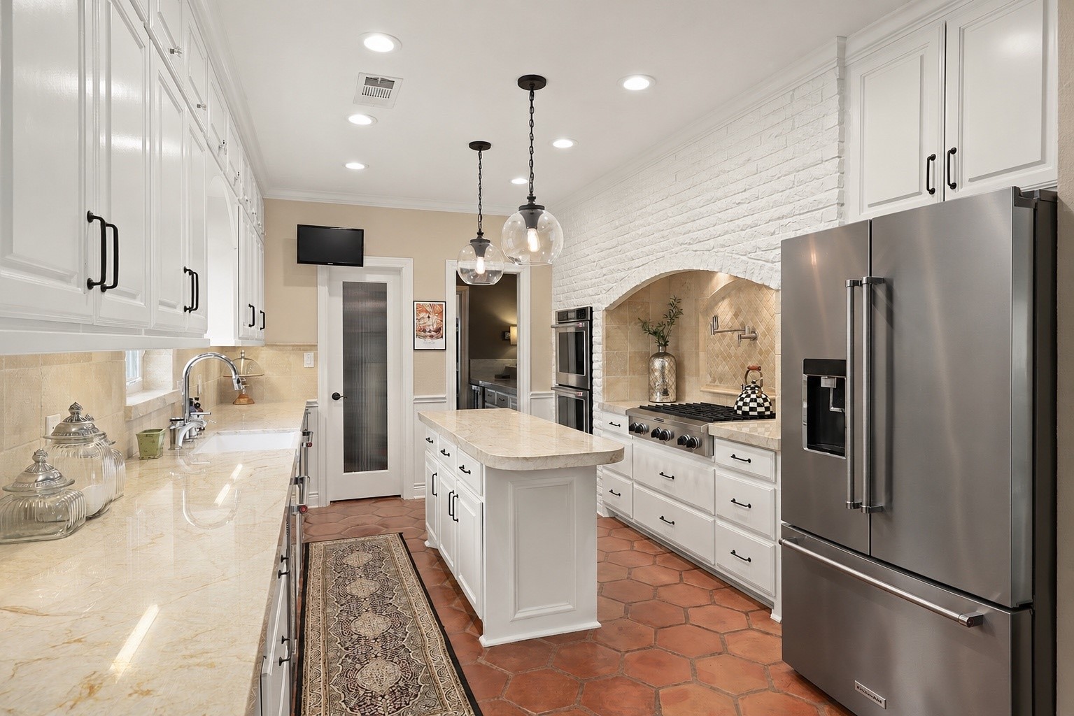 View from the breakfast area looking toward the wet bar, with a spacious walk-in pantry and convenient ice maker to the left. Two beautiful glass pendant lights add elegance, while the television mounted above the pantry conveys with the house.