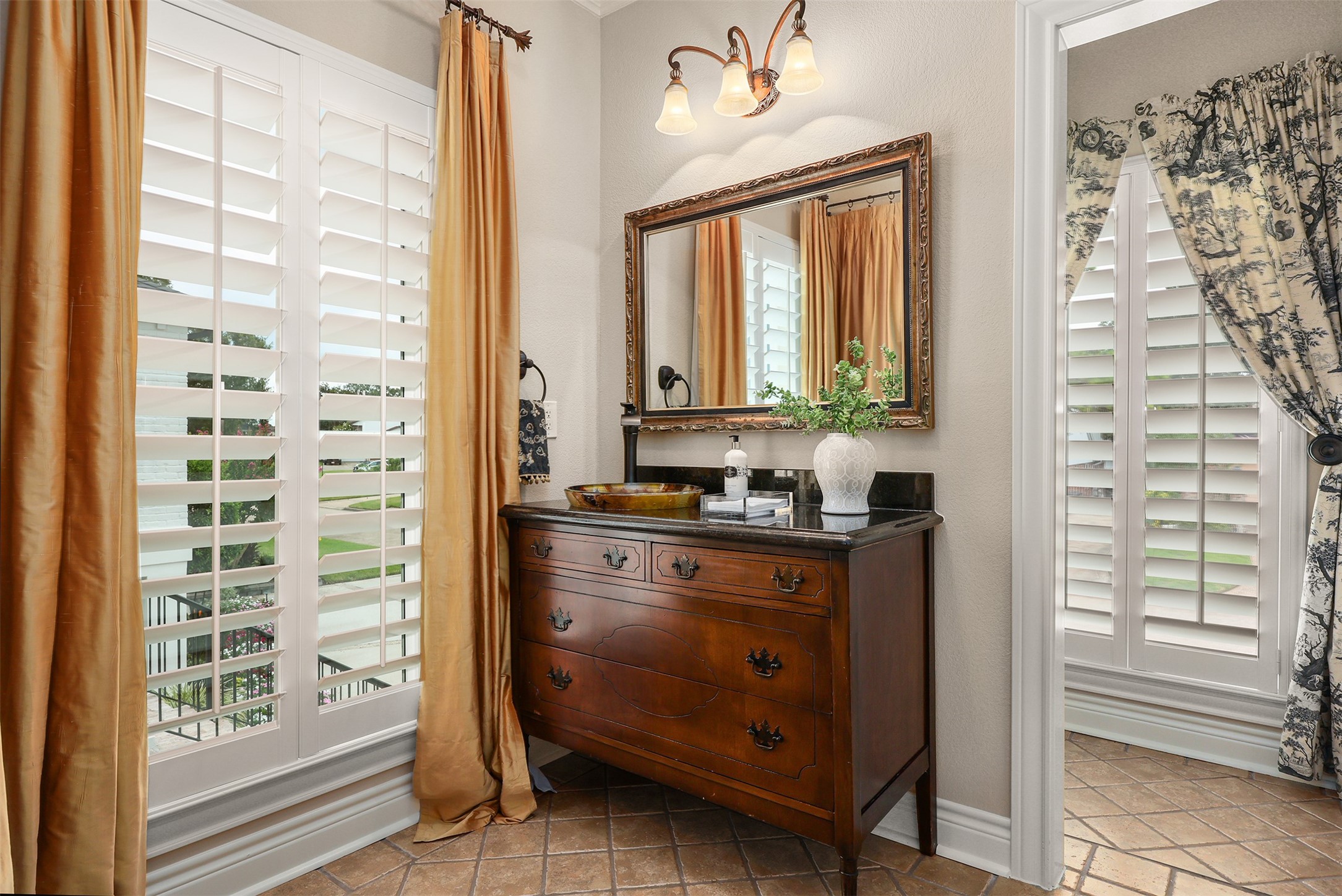 The adjoining full bath to bedroom one features a charming antique furniture-style vanity with a beautiful sink, two windows with plantation shutters, and a separate private toilet area.