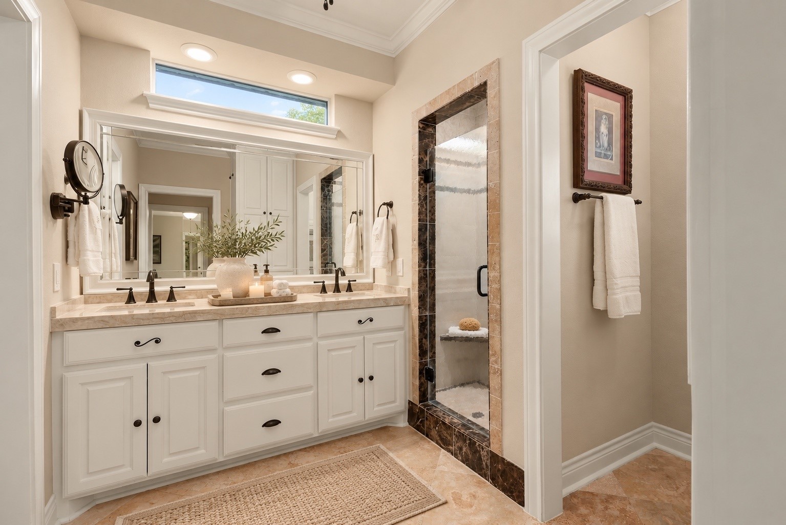 Beautifully appointed primary bath features elegant Taj Mahal countertops, dual sinks, 36" cabinetry, and a white wood-framed mirror. The spacious shower is accented with decorative marble trim and floor-to-ceiling tile, while beautiful travertine flooring adds warmth and timeless elegance throughout.
