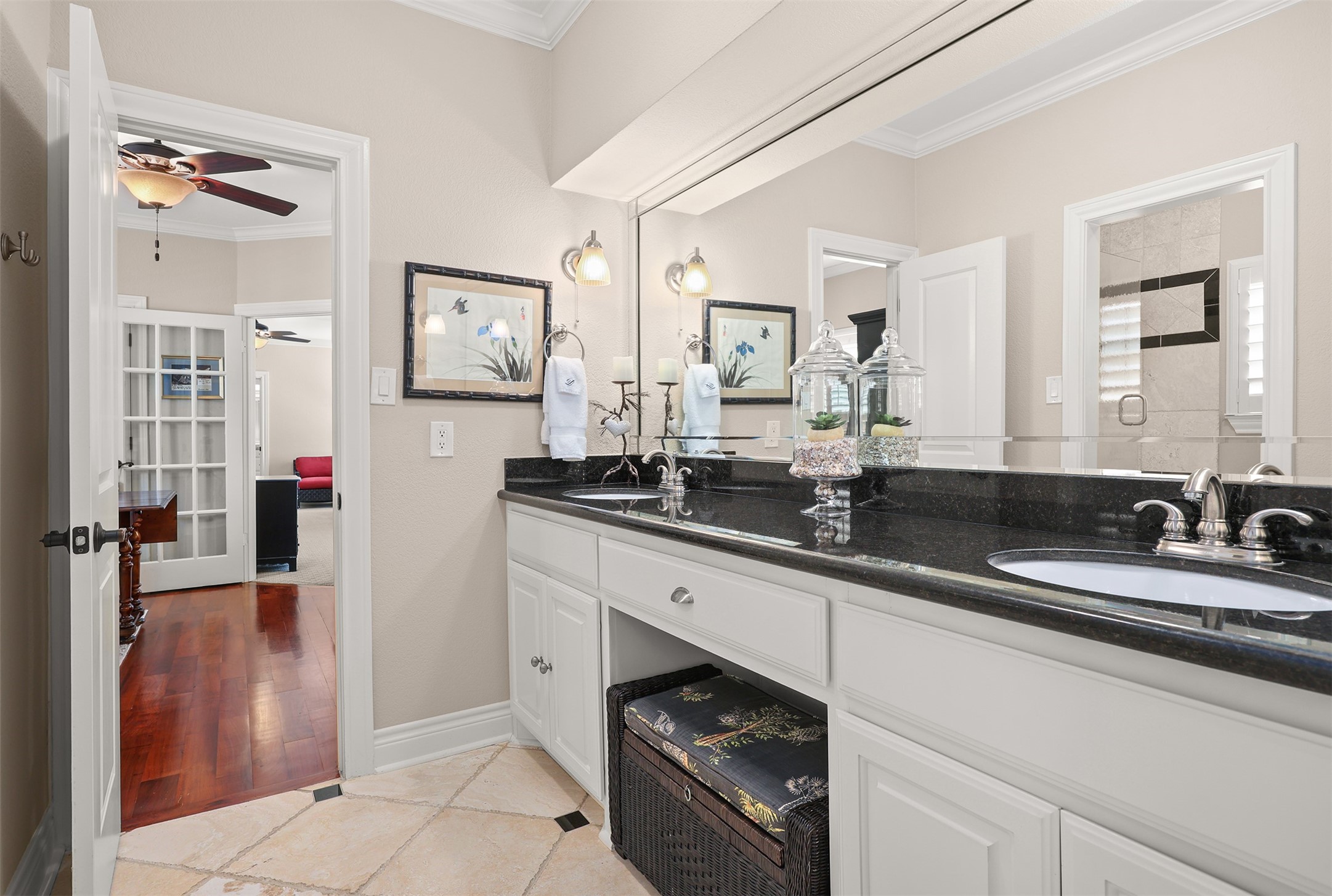 Spacious shared bathroom features beautiful creamy white cabinetry, elegant black granite countertops, double sinks, and an expansive beveled mirror spanning the vanity. Decorative wall sconces provide soft, inviting lighting, while generous counter space and abundant cabinetry offer both comfort and functionality.