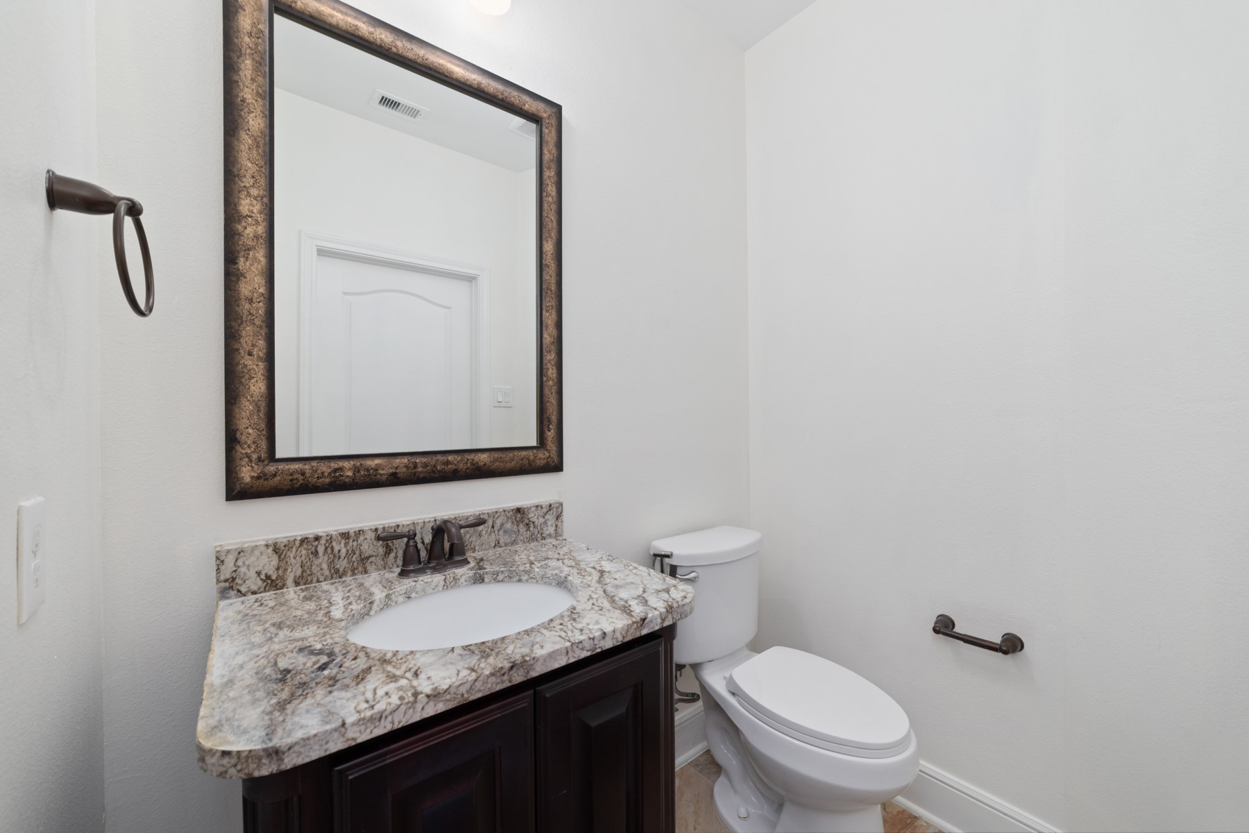 This half bathroom features a sleek design with a granite countertop, and dark wood vanity.
