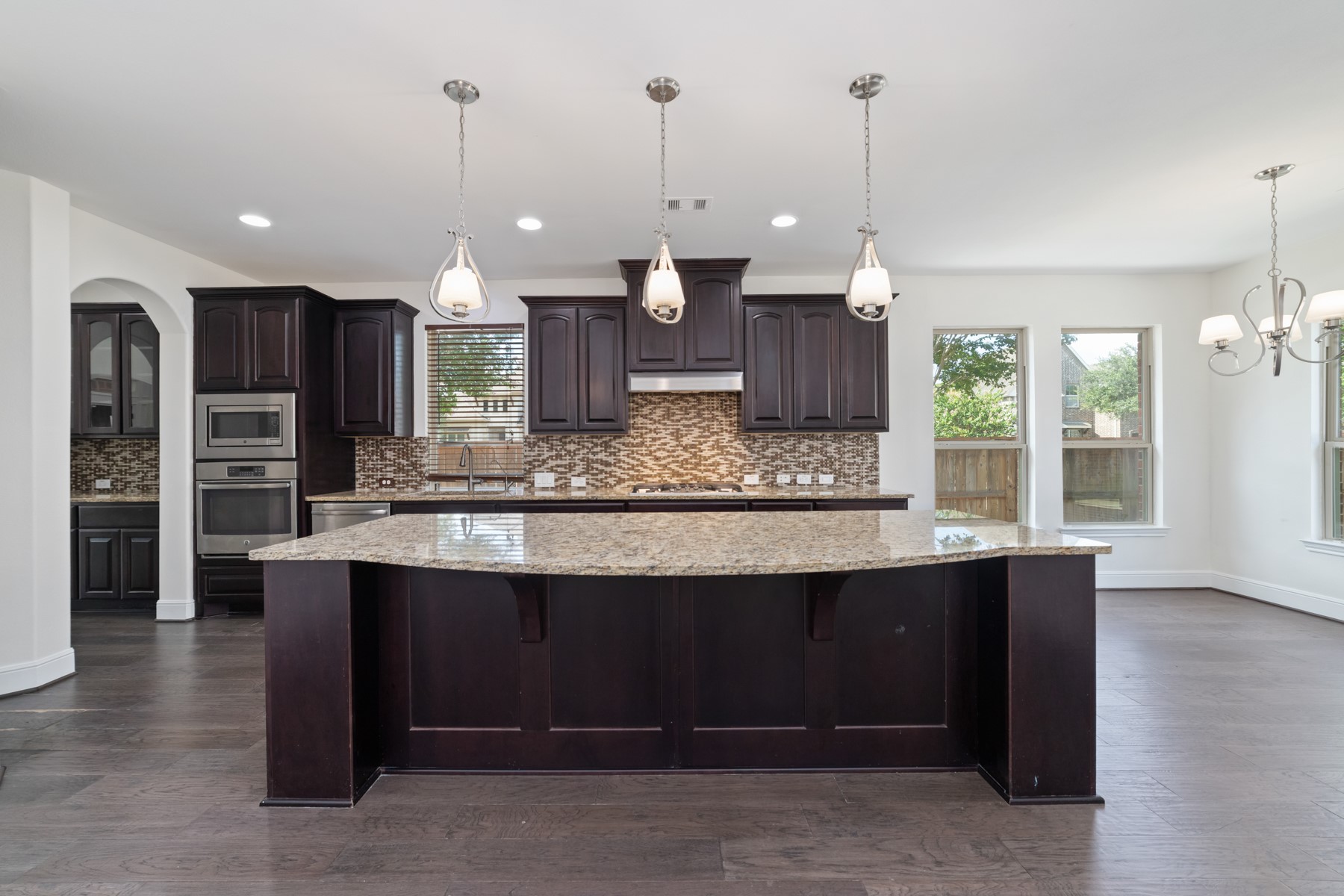 This modern kitchen features elegant dark wood cabinetry, a large center island, and stainless steel appliances.