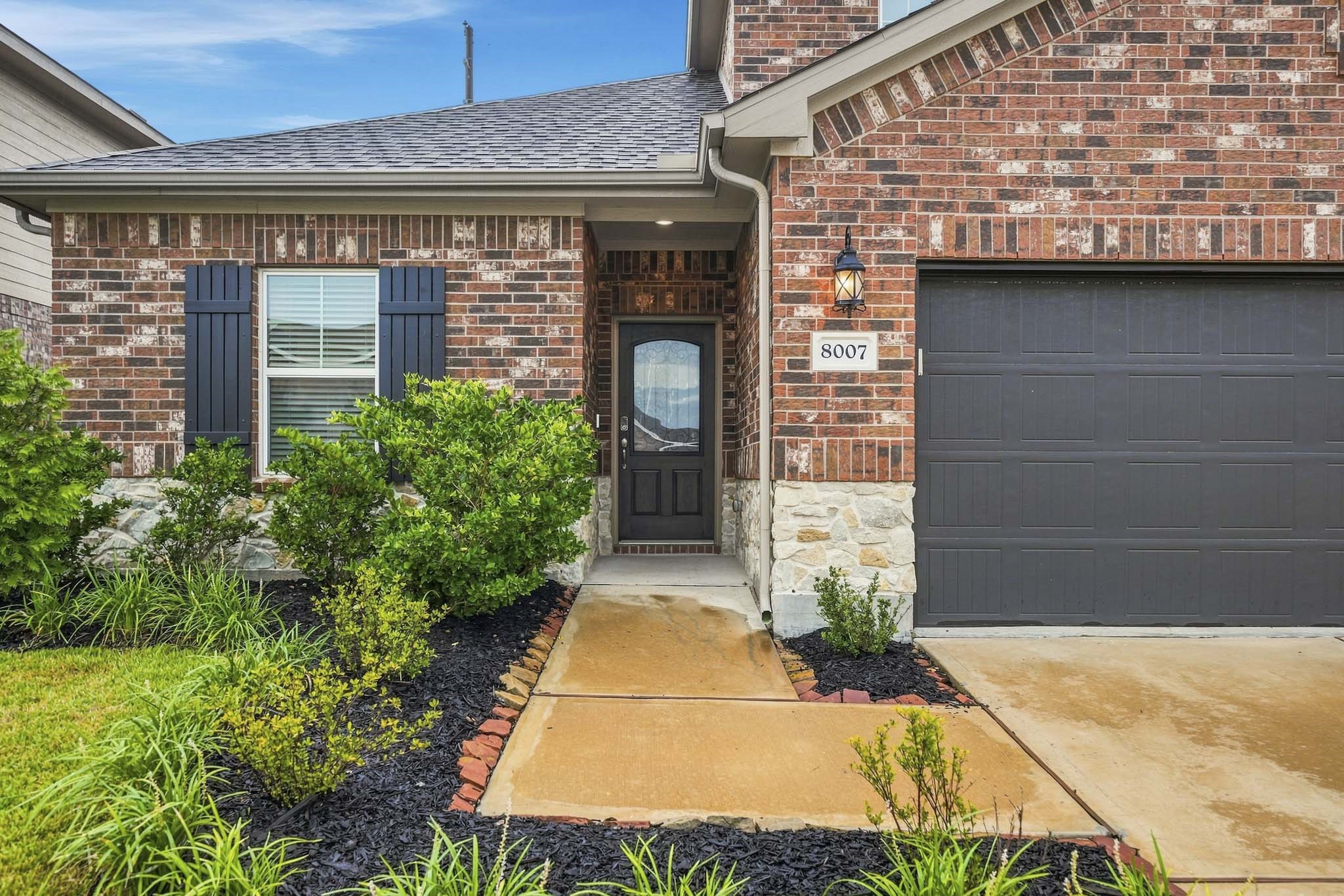 Charming brick and stone exterior with elegant dark accents, a neatly landscaped front yard, and a welcoming entryway.