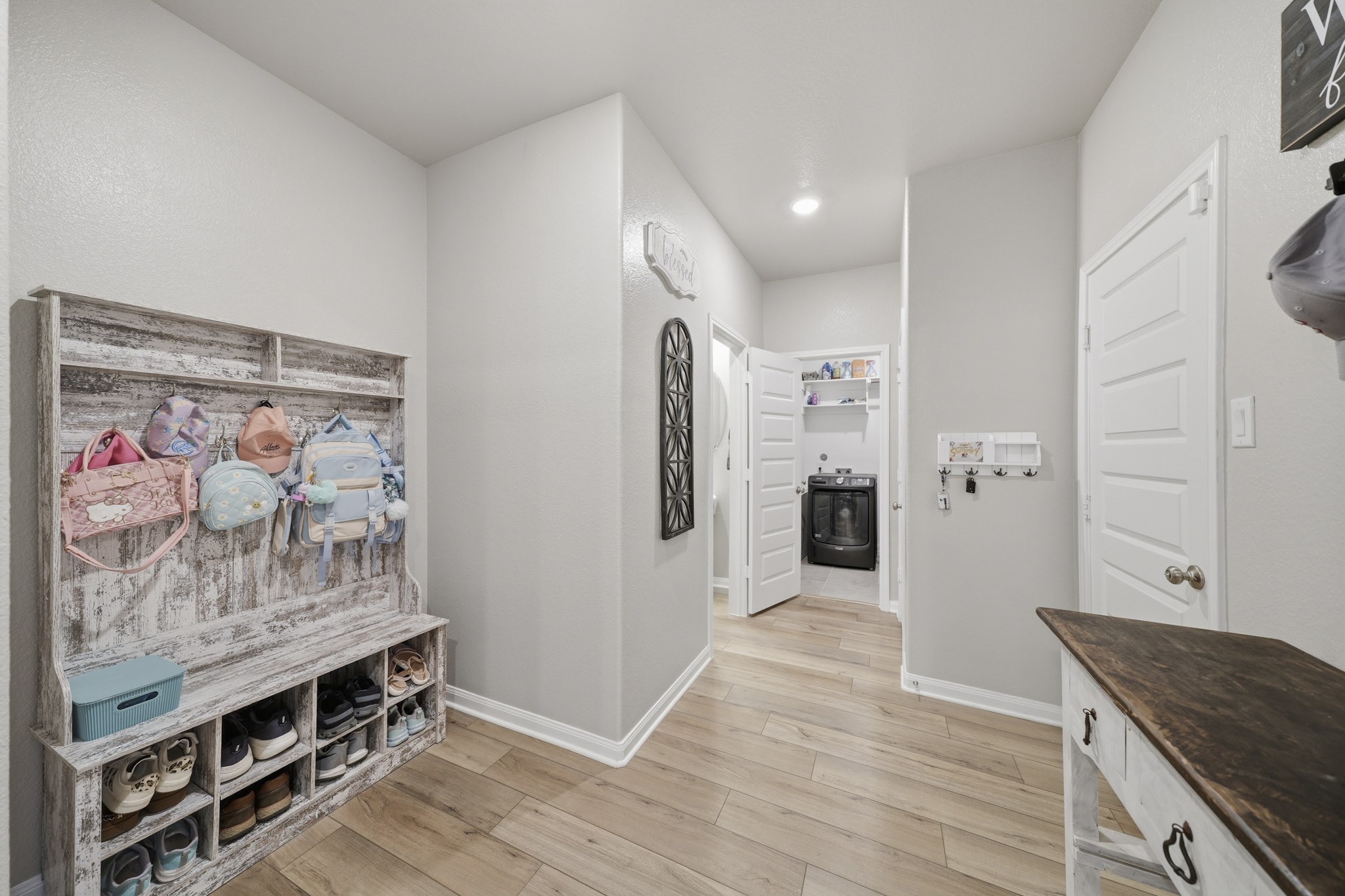 Charming mudroom featuring a rustic shoe storage bench and convenient hooks for bags, leading to a modern laundry room with ample shelving.
