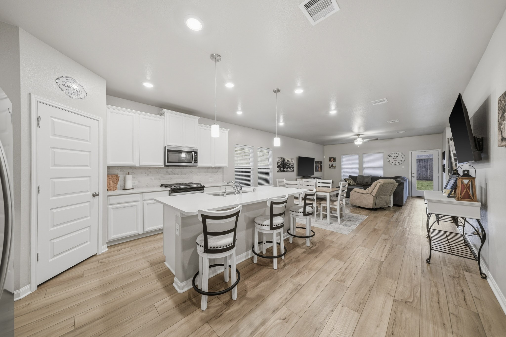Spacious open-concept kitchen and living area featuring modern white cabinetry, a large island with seating, and sleek stainless steel appliances. The adjoining living space offers comfort with plush seating and ample natural light, perfect for entertaining.