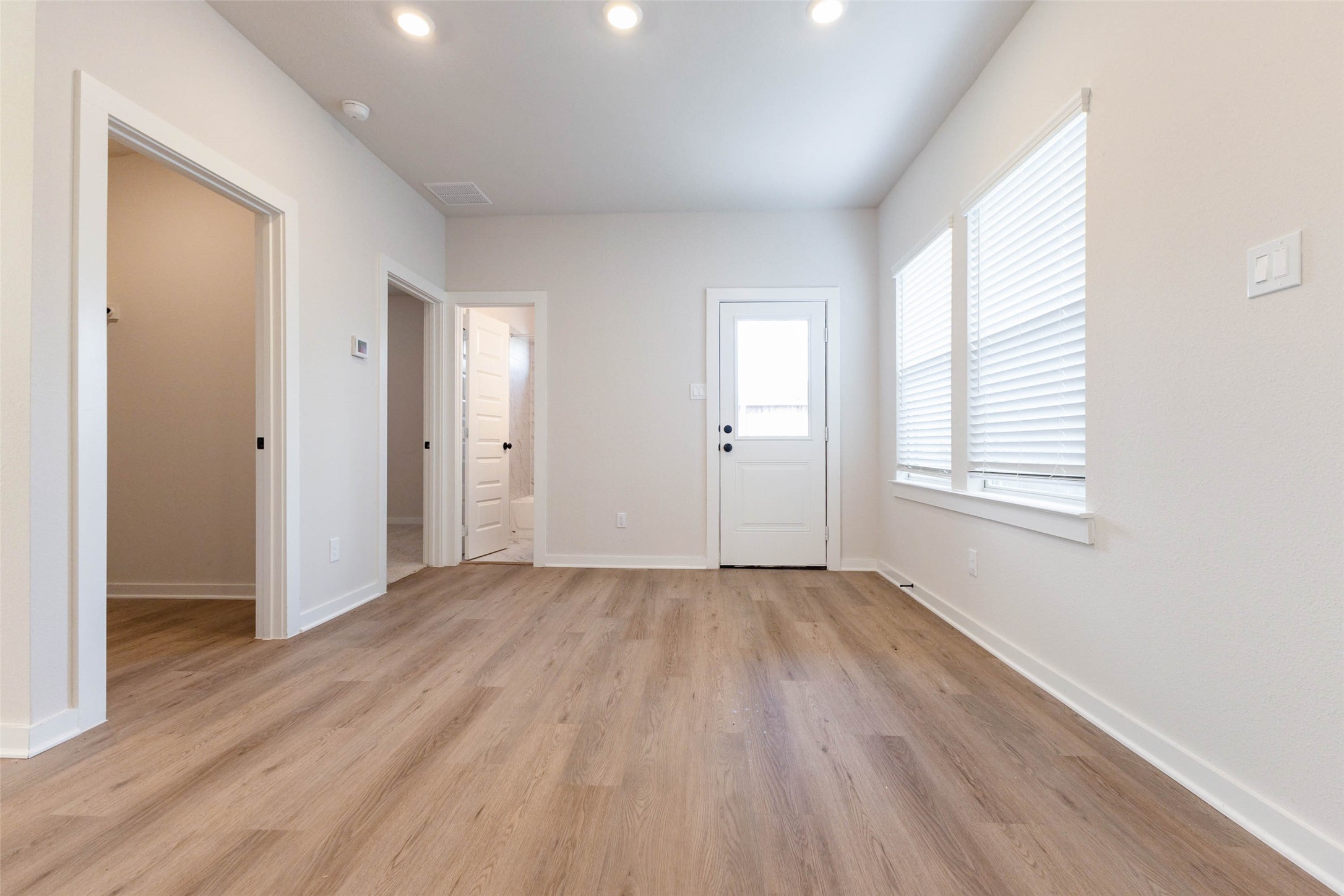 This hallway and utility area connects the main living space to the back door and secondary rooms, keeping everyday traffic away from the kitchen. A window lets in natural light, and the wood-look floors continue the same clean, low-maintenance finish used throughout. Doorways lead off to the bedroom wing and bath, giving the floor plan an easy flow and a bit of separation for quiet.