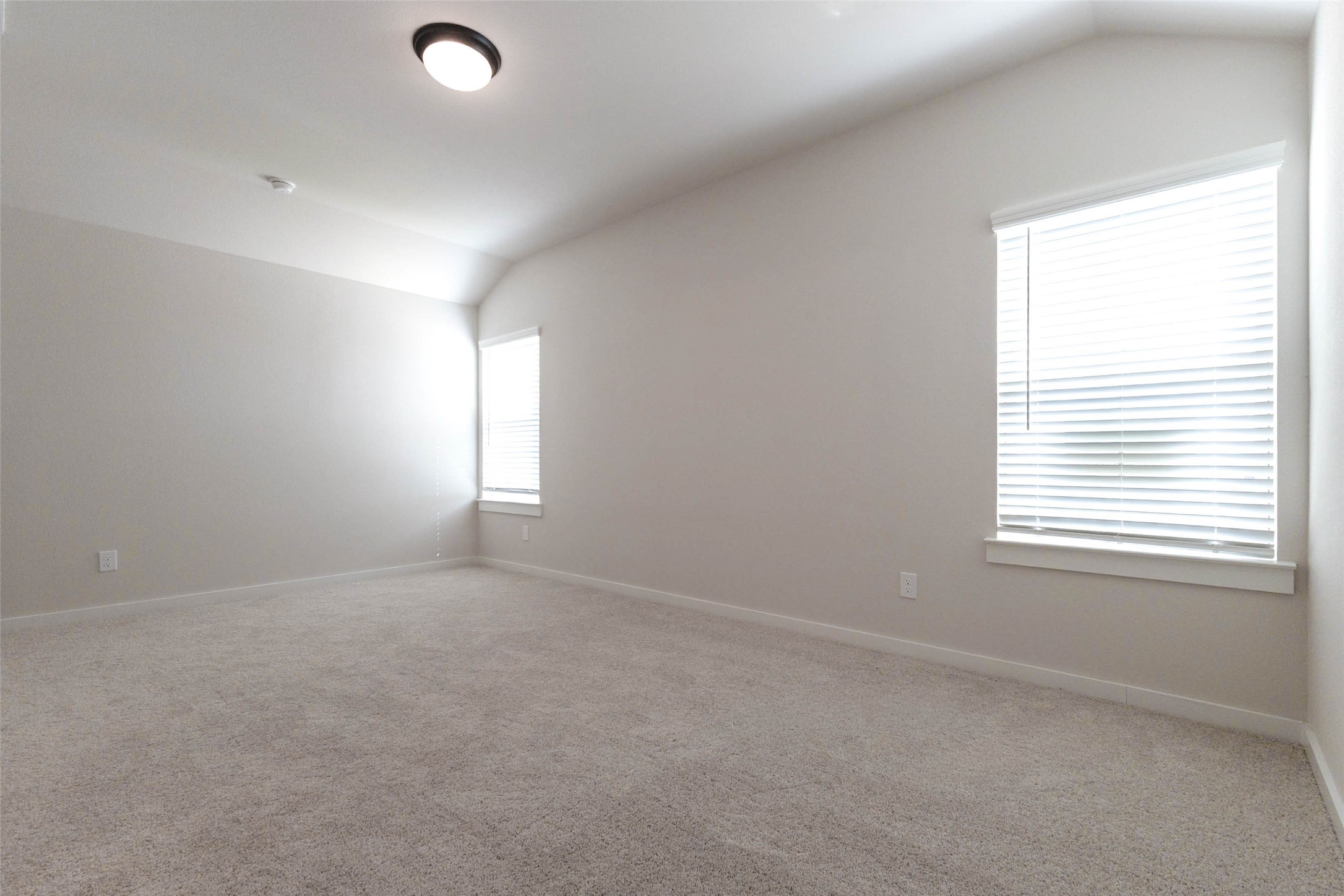 This third bedroom features a large window with blinds, soft carpet and a vaulted ceiling that adds volume. There is plenty of wall space for a bed, dresser and desk, and a ceiling light keeps it bright at any hour. Whether it becomes a child's room, a guest room or a hobby space, it offers comfort, light and flexibility that fits whatever life brings next.