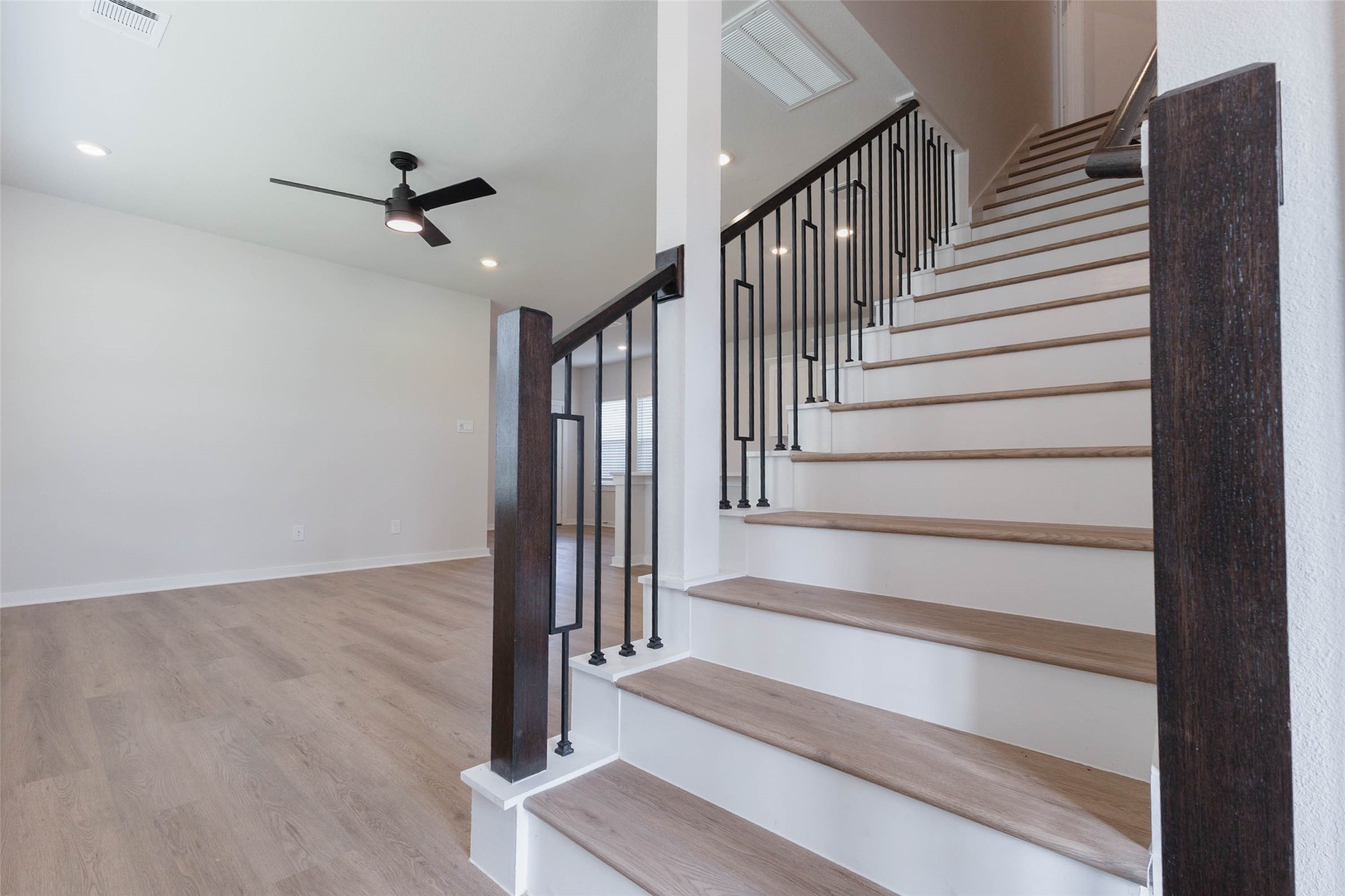 Wood-treaded stairs with black iron spindles and a rich dark newel post make the staircase a design feature as well as the path to the second floor. Natural light spills across the steps from above, and a ceiling fan keeps the landing comfortable. The open stair keeps the main floor feeling connected to the upper level and adds a custom-built look you rarely see at this price.