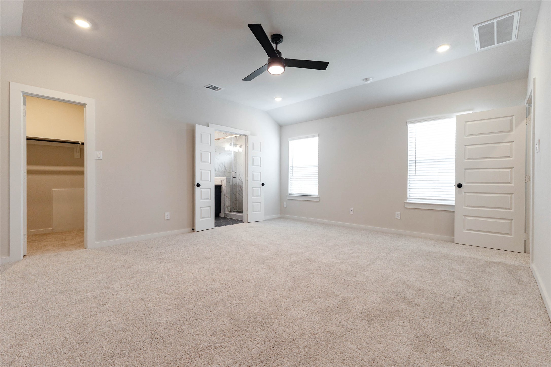 The primary bedroom is large enough for a king bed, seating area and dressers, with a ceiling fan and recessed lights for easy comfort. Double doors open to the spa-style bath, and another door leads to a walk-in closet, so getting ready is simple and private. Two windows with blinds bring in plenty of natural light, and the plush carpet is gentle underfoot first thing in the morning.