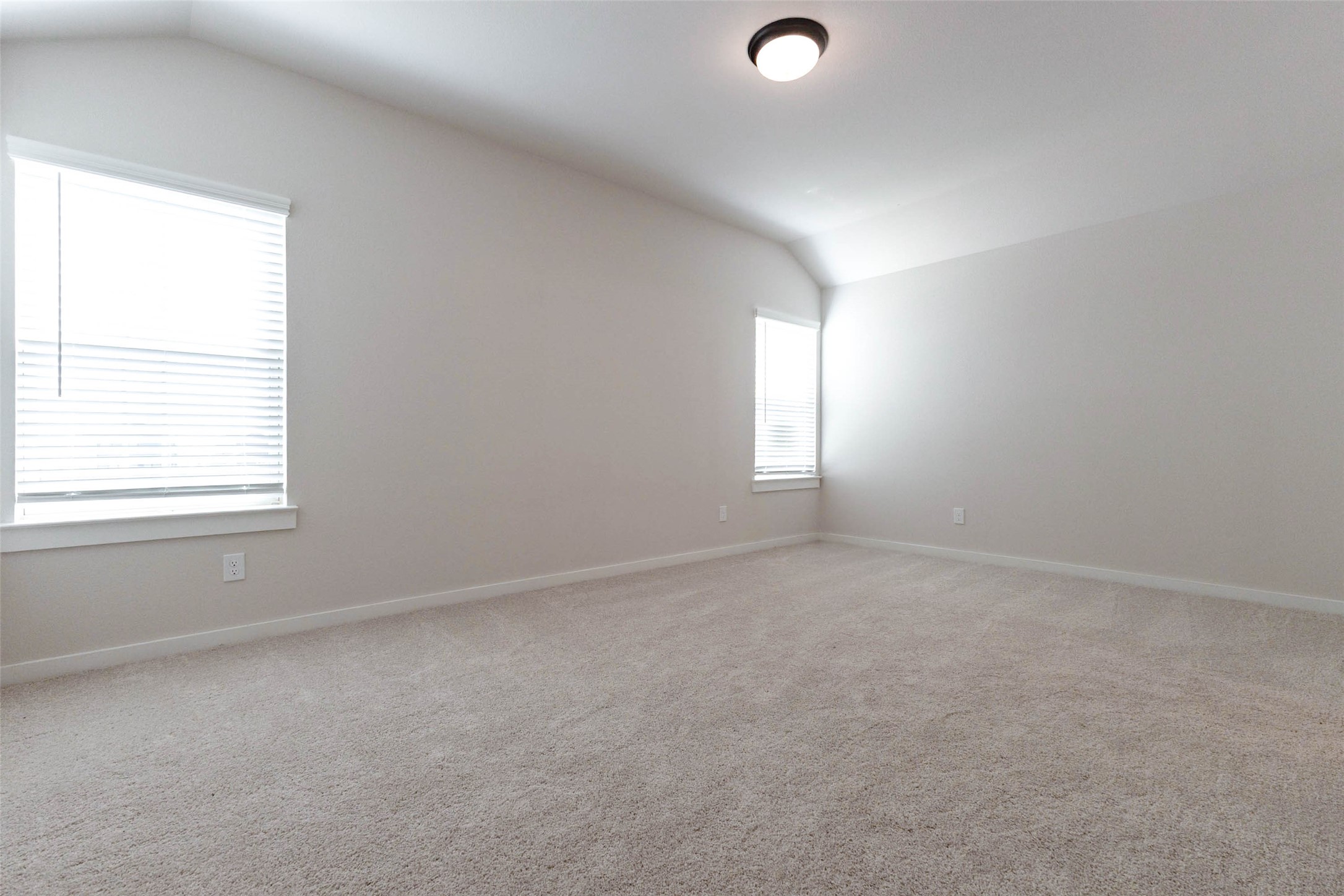 This bedroom has a vaulted ceiling that makes the room feel taller, and a large window with blinds fills it with natural light. Soft neutral carpet and fresh paint make it a blank canvas for a nursery, kids' room, guest suite or work-from-home space. A flush-mount ceiling light and plenty of wall space mean furniture placement is easy no matter how you use it.