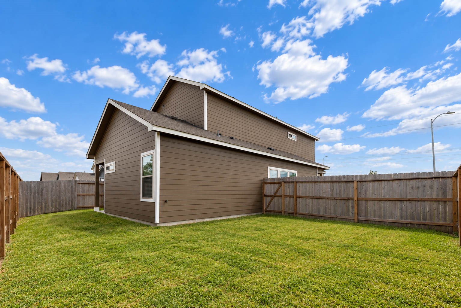 A final look at the backyard shows the full privacy fence, the neat lawn and the home's side and rear exterior with its durable siding and neutral color. With room to roam and an open sky above, it is a great setting for pets, play and entertaining. Combined with the community pool, splash pad, playground and trails nearby, outdoor living is easy here.