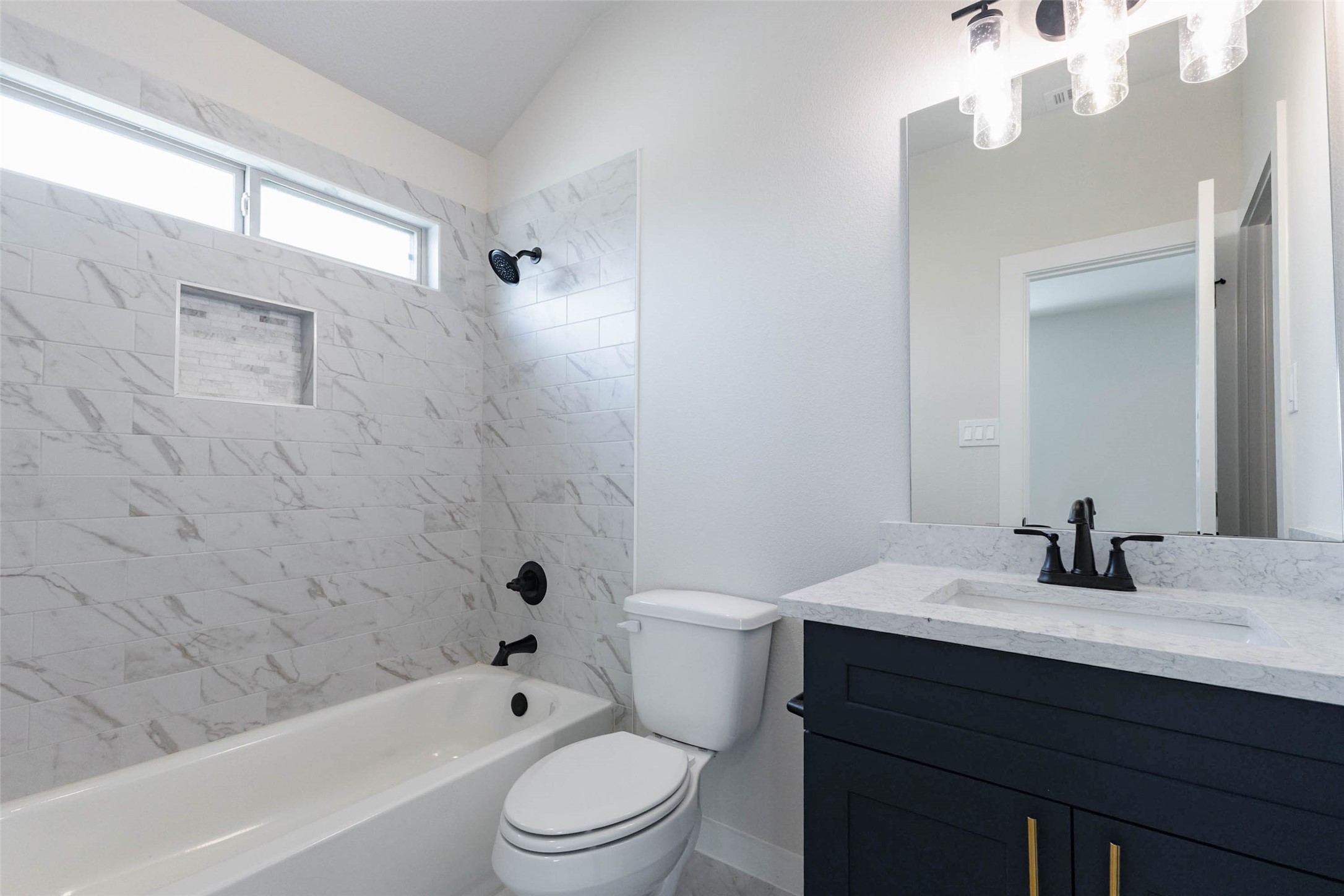 Another full bath has a tub-shower wrapped in marble-look tile with a built-in shelf niche, a high transom window and matte black fixtures. A navy vanity with a quartz top matches the primary bath, giving the home a cohesive, designer feel. A full bathroom serving the extra bedrooms keeps mornings running smoothly and gives guests their own comfortable space.